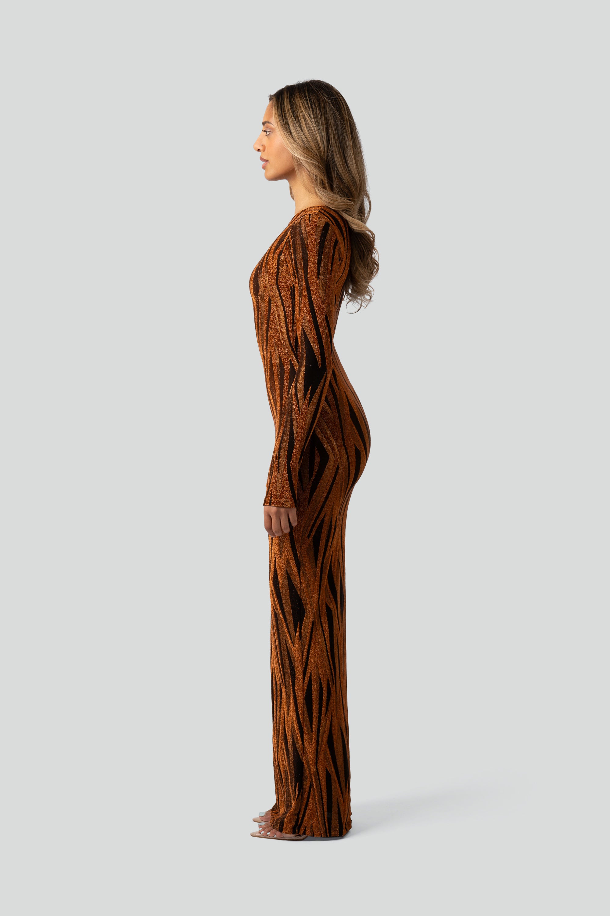 Side view of a woman wearing an orange and black patterned dress on a gray background