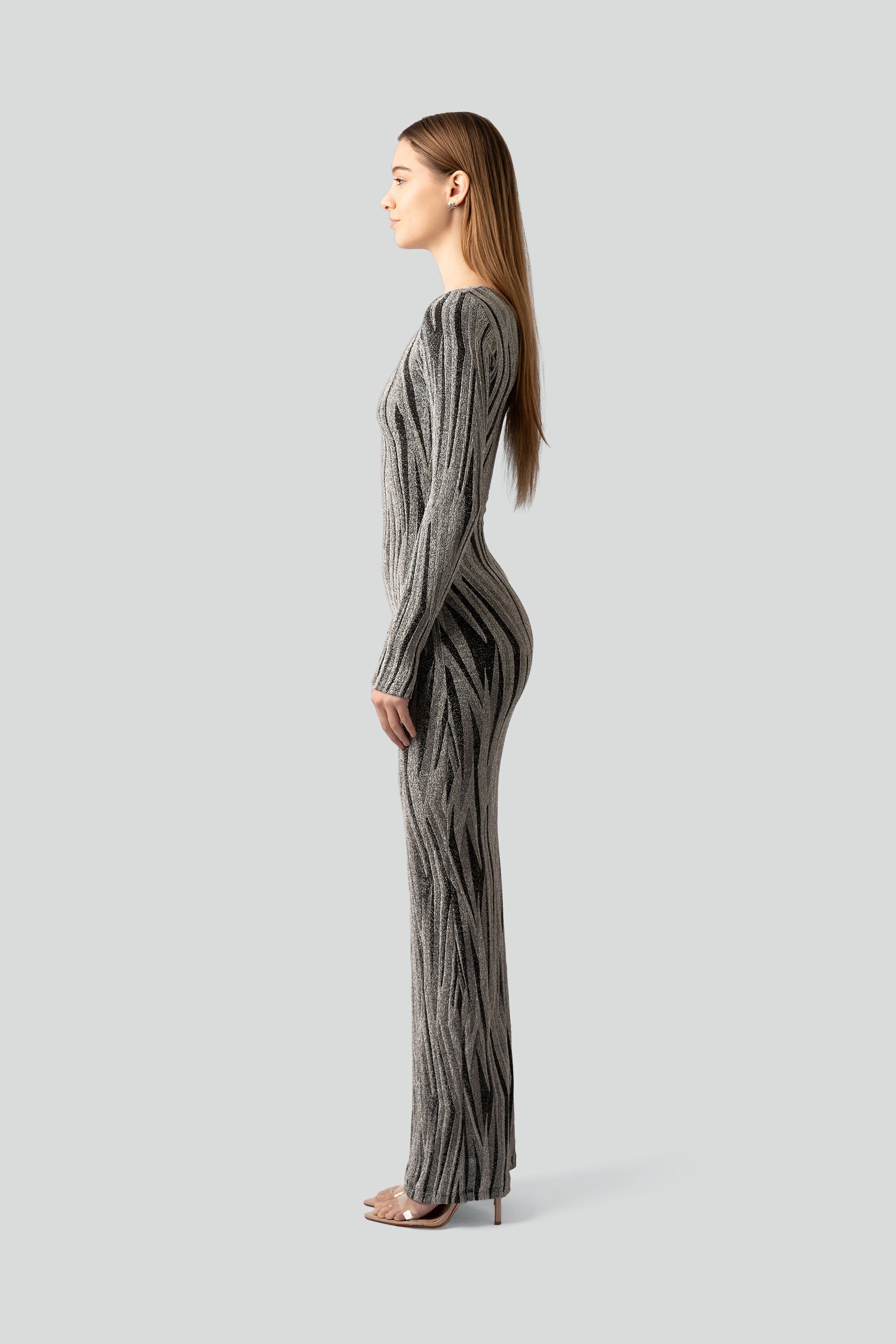 Side view of a woman wearing a silver and black patterned dress on a gray background