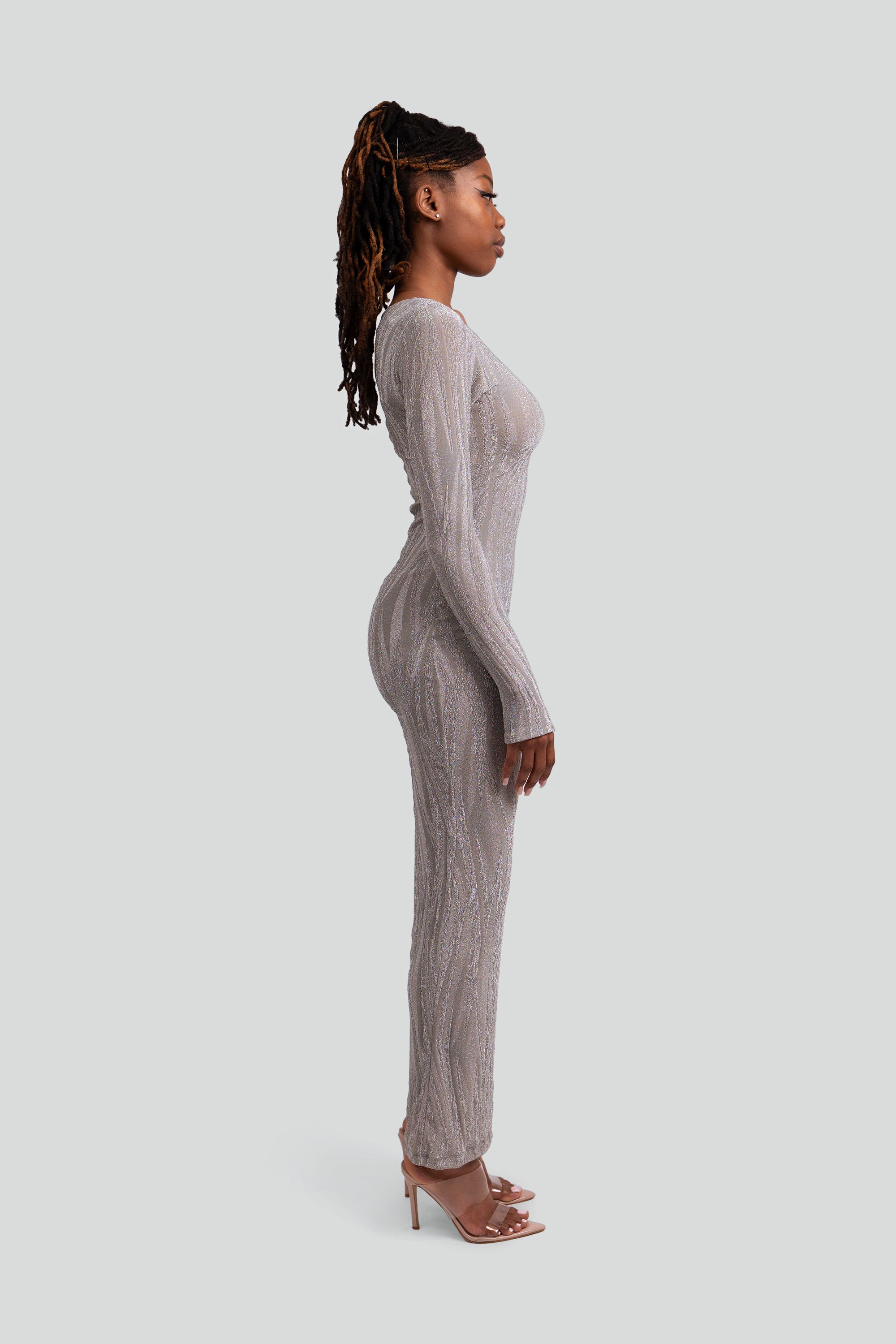 Side view of a woman wearing a silver patterned dress on a gray background
