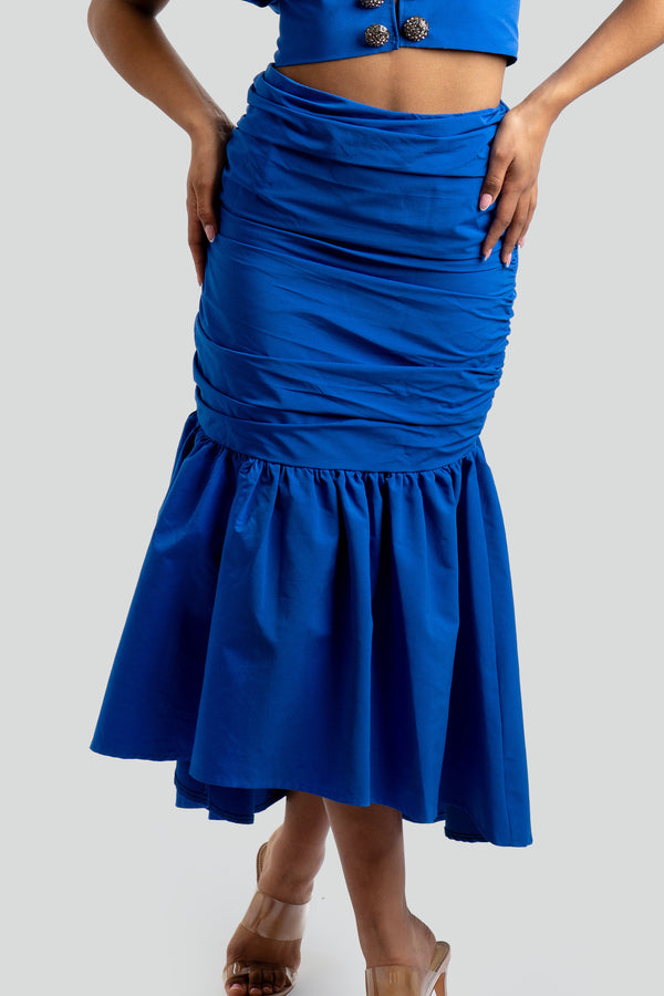 High-waisted form-fitting maxi skirt featuring meticulous body-sculpting ruching and an asymmetrical tiered ruffle hem that falls into a voluminous flounce