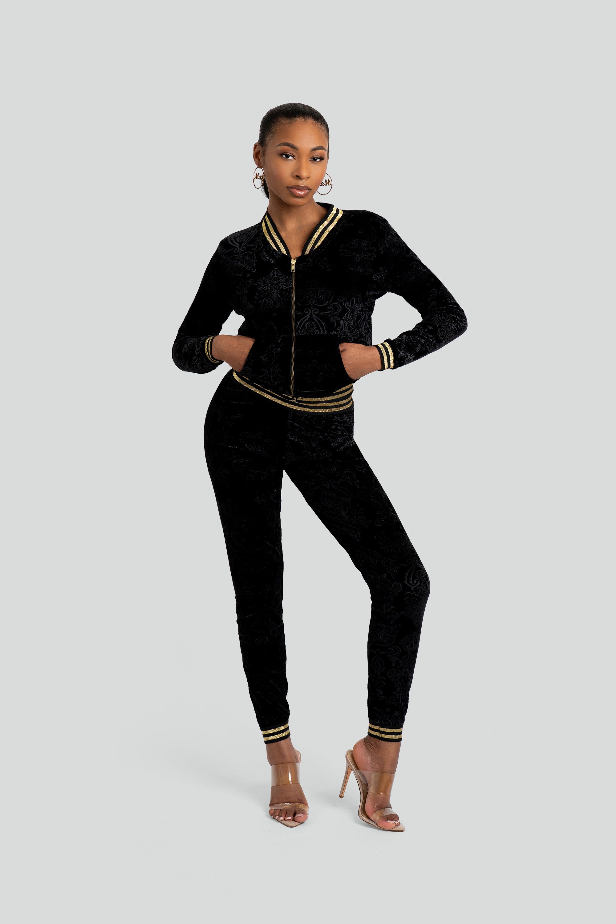 Woman wearing a black velour tracksuit with floral patterns and gold trim on a white background
