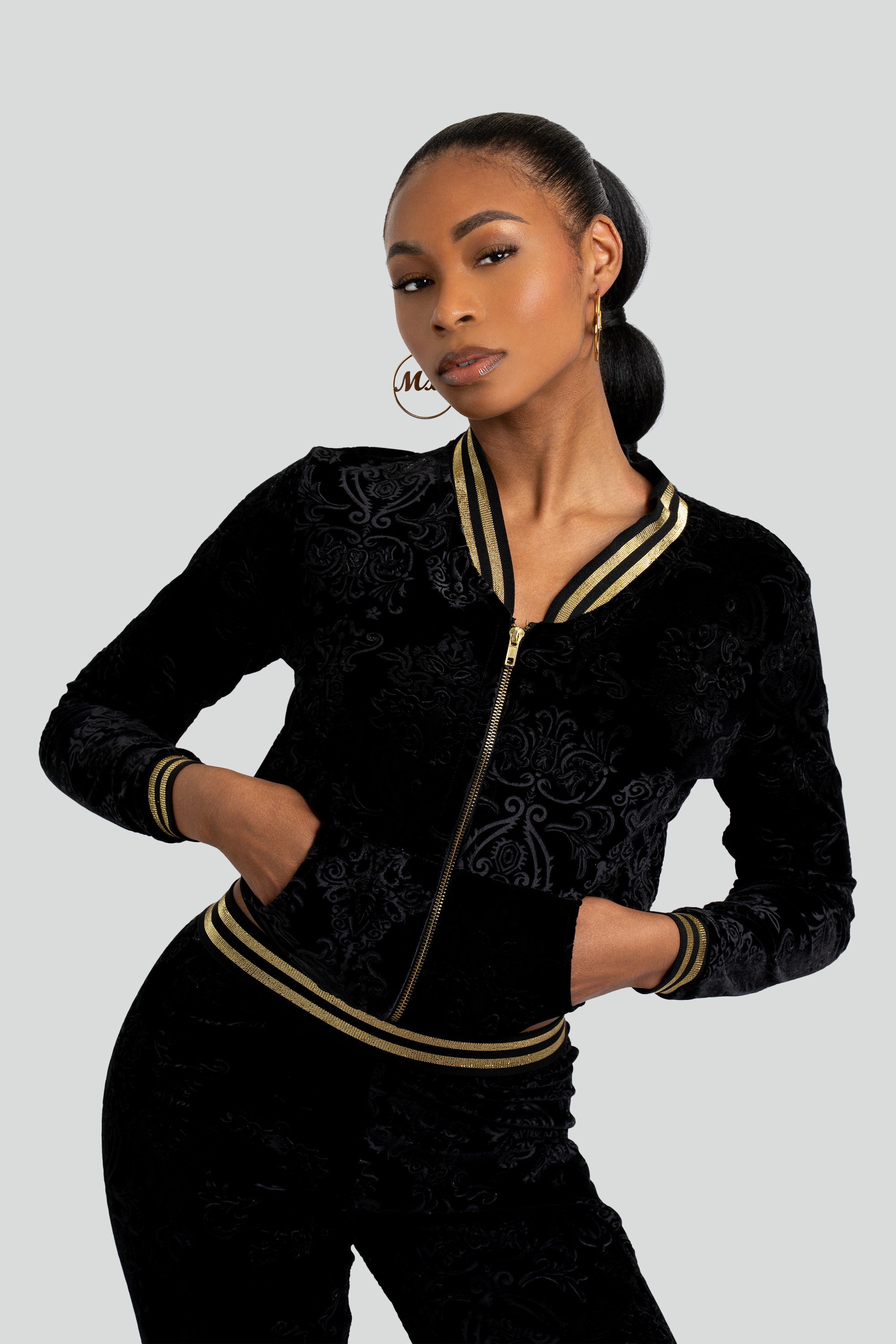 Woman wearing a black velour tracksuit with floral patterns and gold trim on a white background