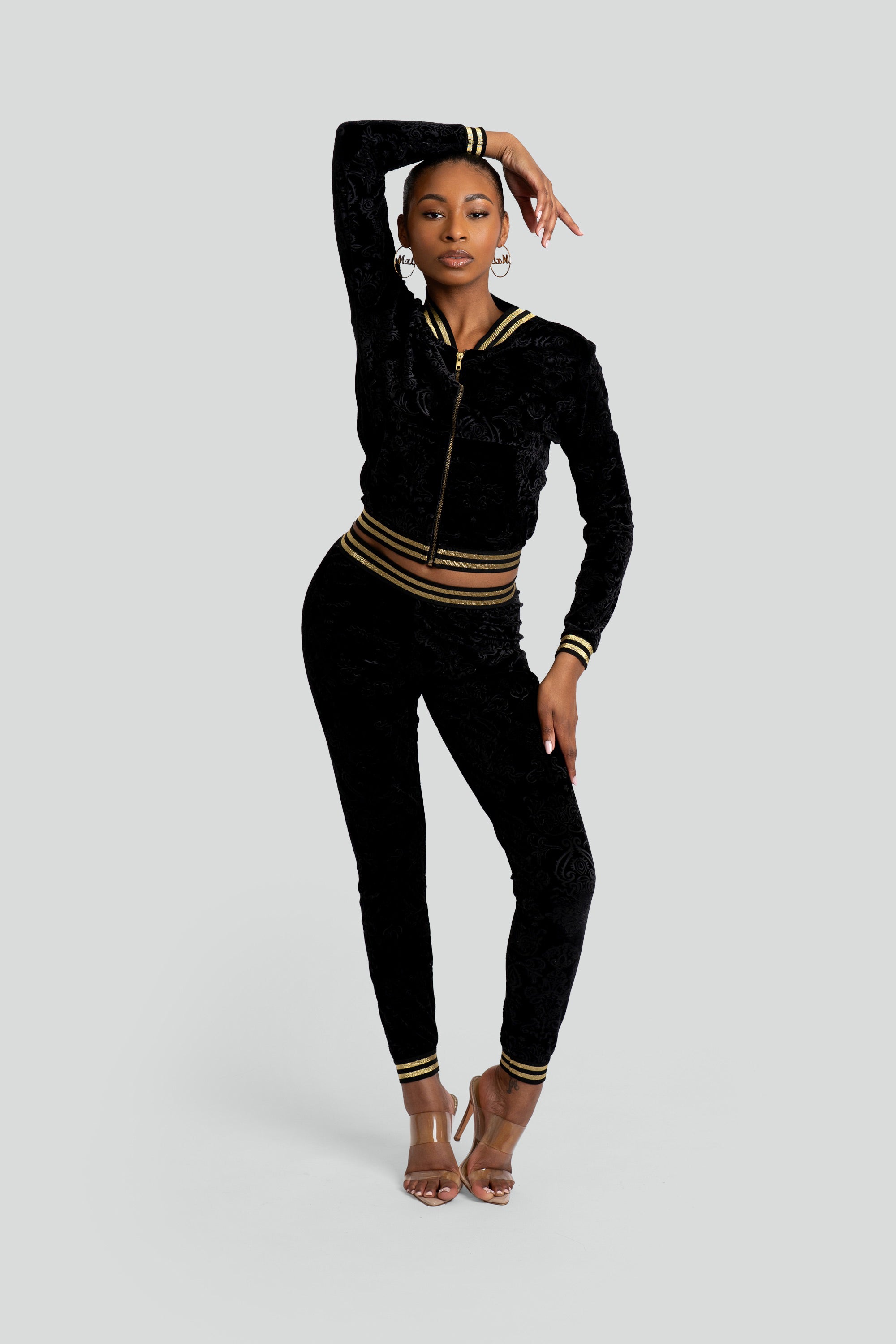 Woman wearing a black velour tracksuit with floral patterns and gold trim on a white background