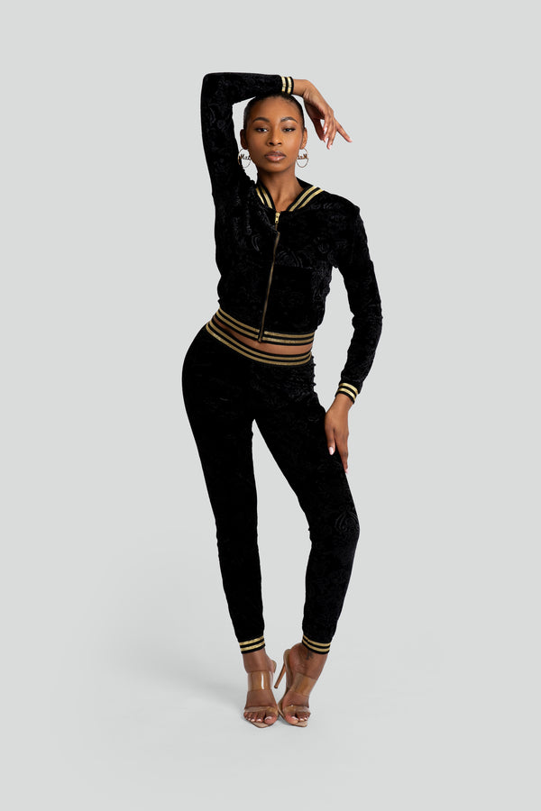 Two-piece women's luxury streetwear set made of plush black velour embossed with subtle regal motifs, featuring a zip-up jacket and matching joggers