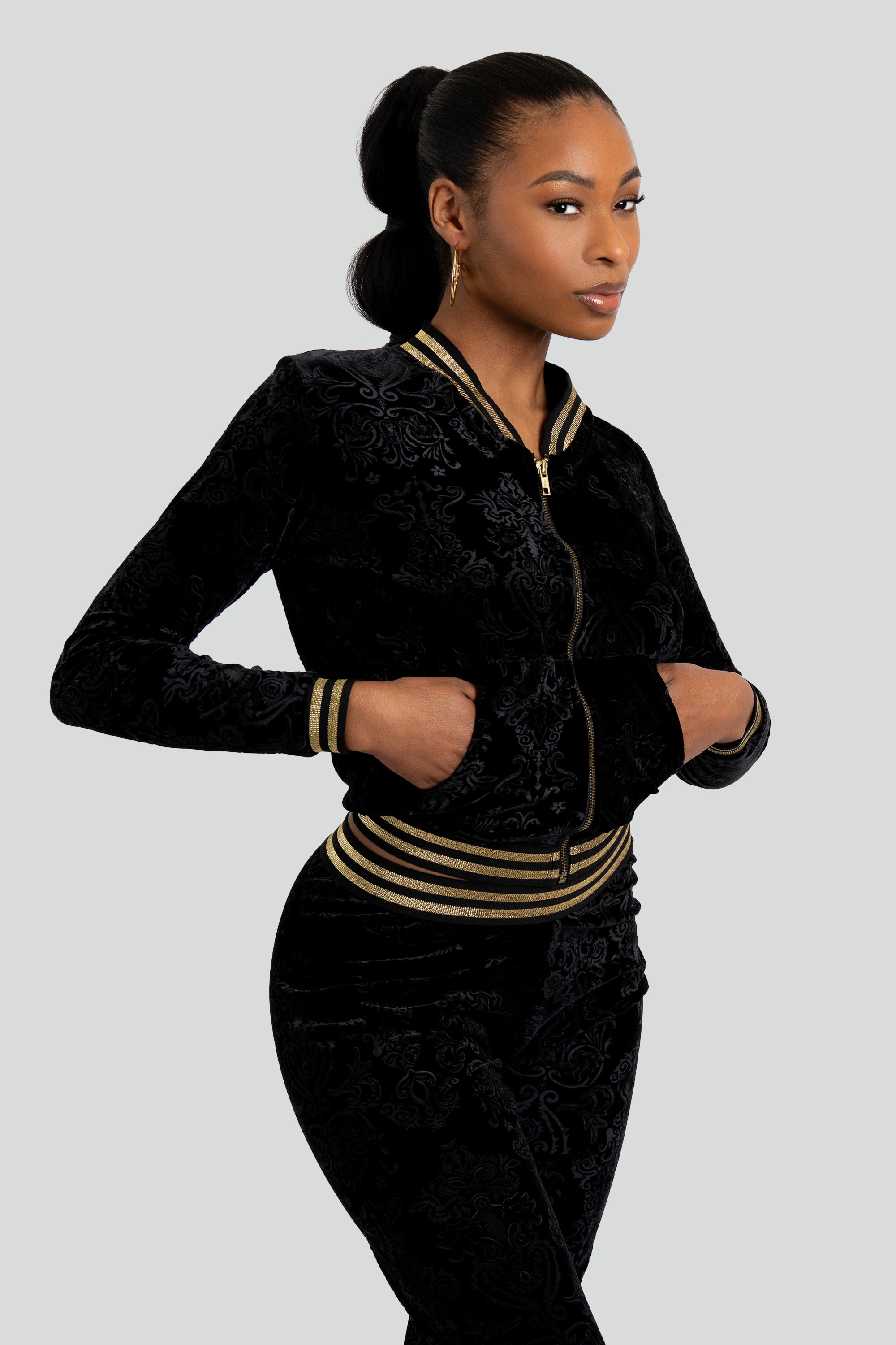 Woman wearing a black velour tracksuit with floral patterns and gold trim on a white background