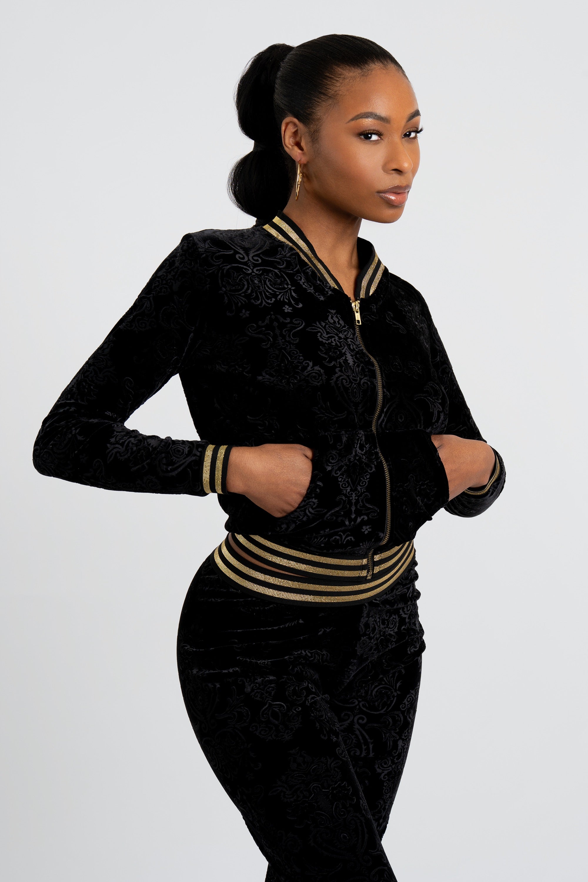 Woman wearing a black velour tracksuit with floral patterns and gold trim on a white background