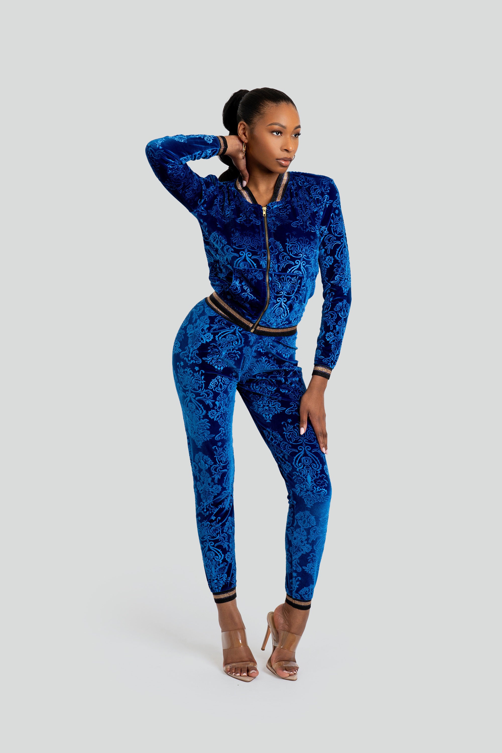 Woman wearing a blue velour tracksuit with floral patterns and gold trim on a white background