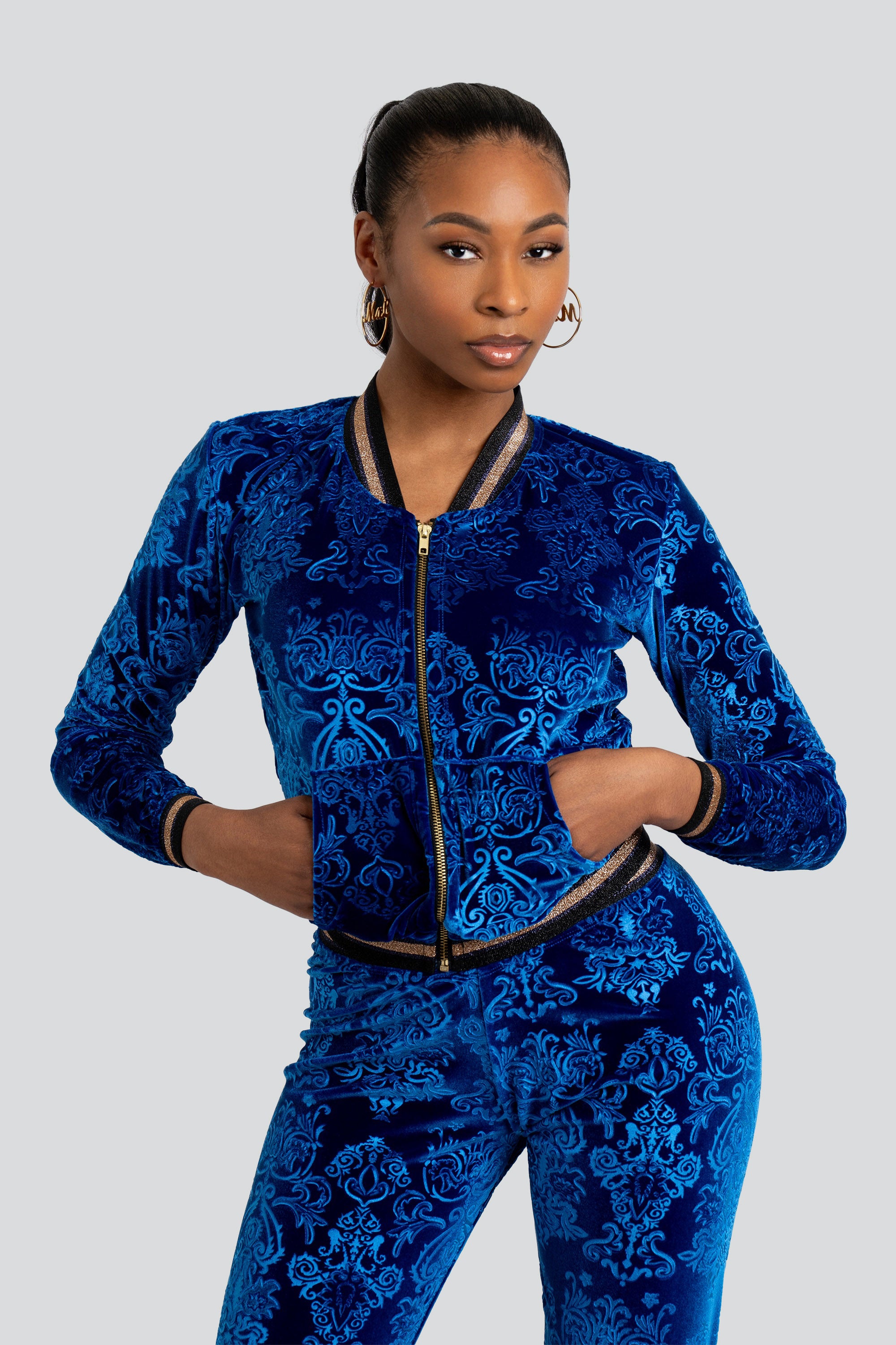 Woman wearing a blue velour tracksuit with floral patterns and gold trim on a white background