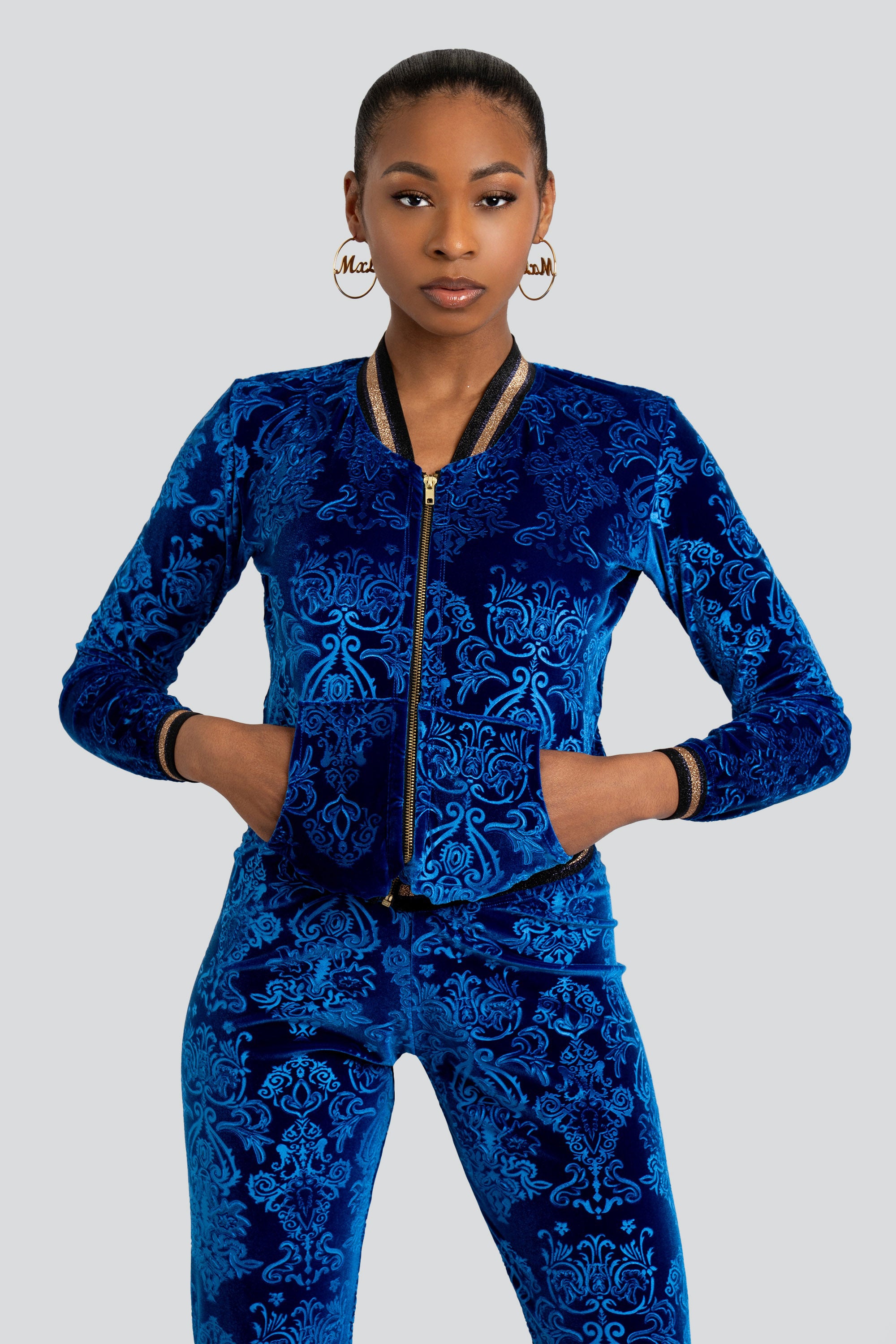 Woman wearing a blue velour tracksuit with floral patterns and gold trim on a white background