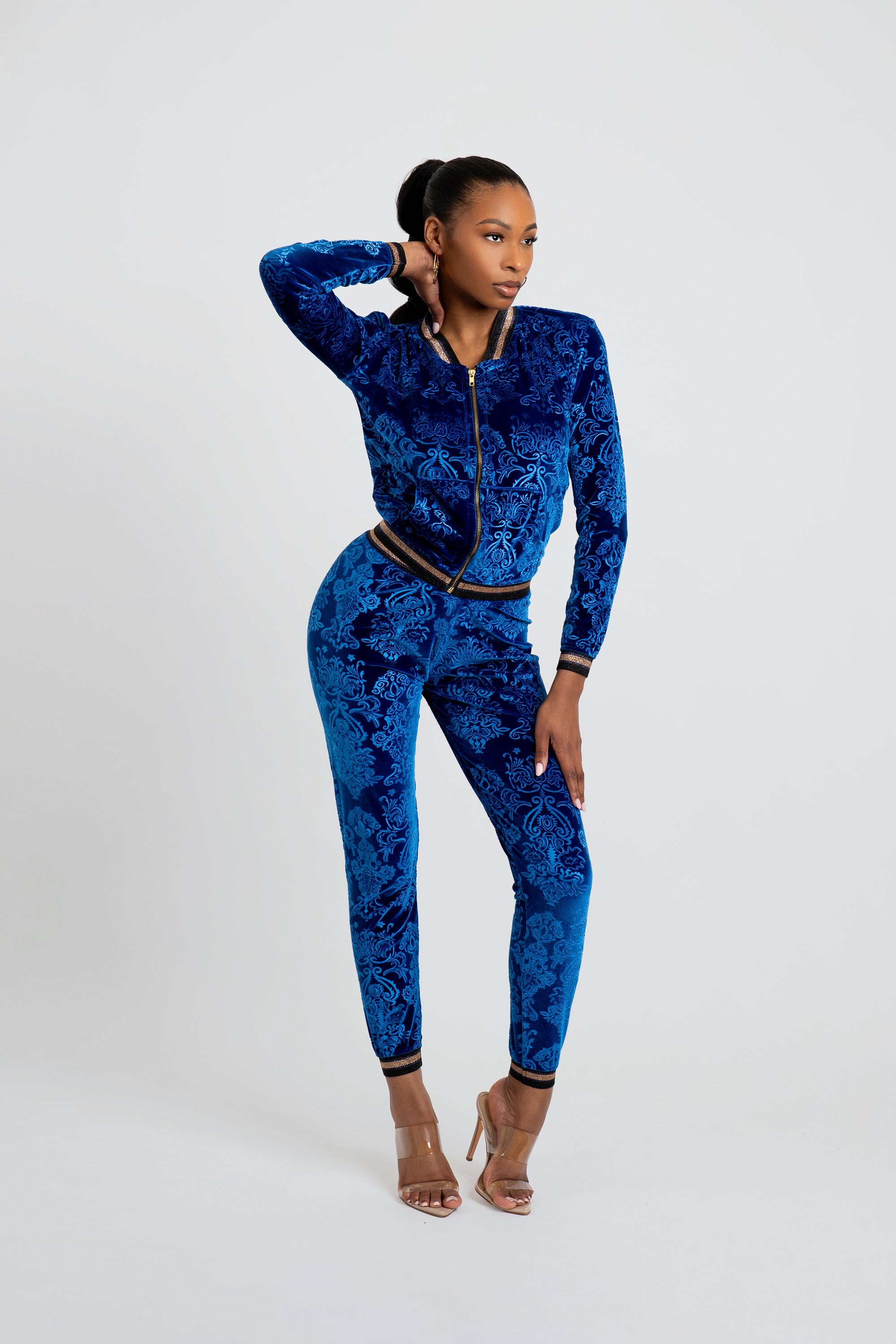 Woman wearing a blue velour tracksuit with floral patterns and gold trim on a white background
