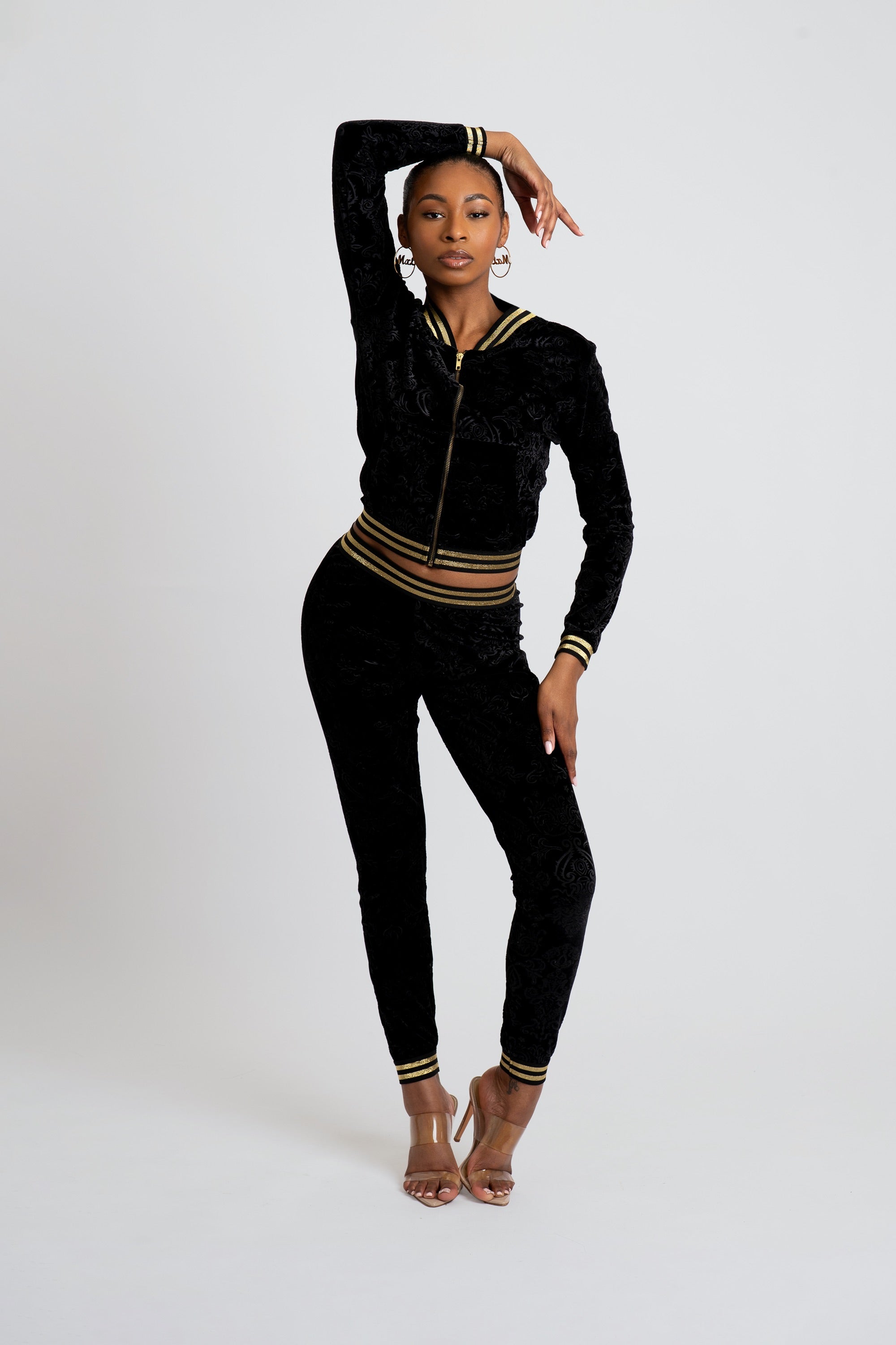 Woman wearing a black velour tracksuit with floral patterns and gold trim on a white background