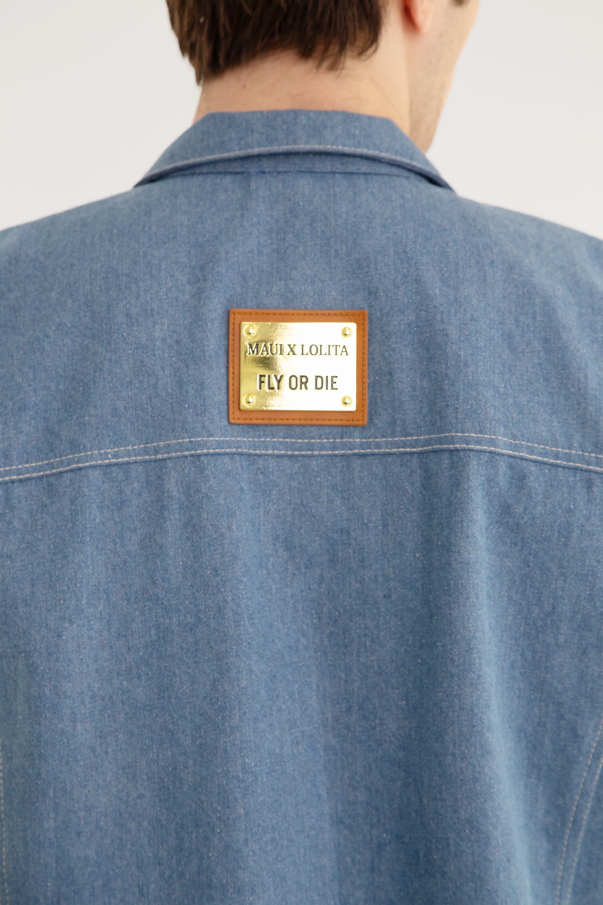 Blue denim jacket with a gold brand label on the back