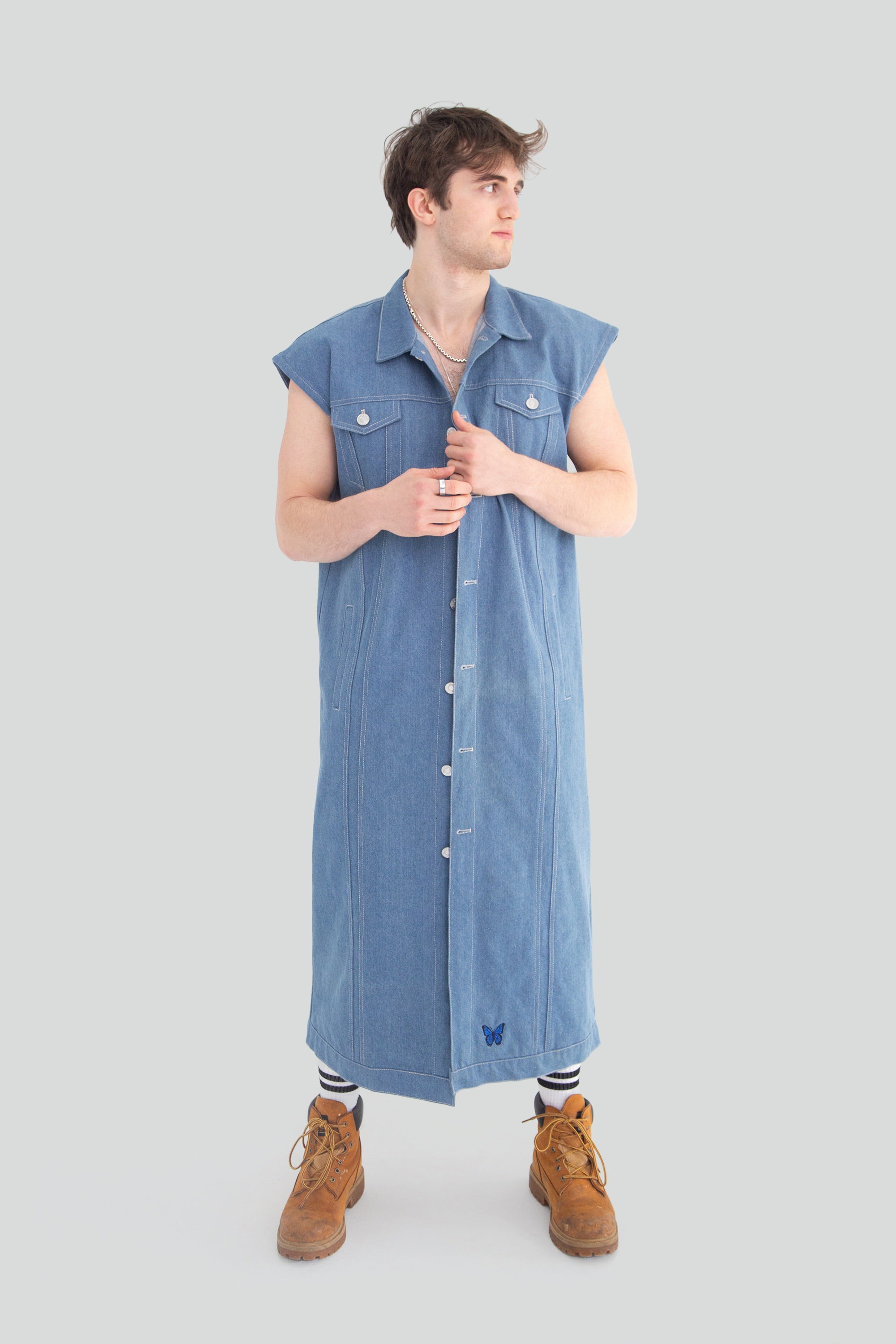 Person wearing a long blue denim vest on a plain background