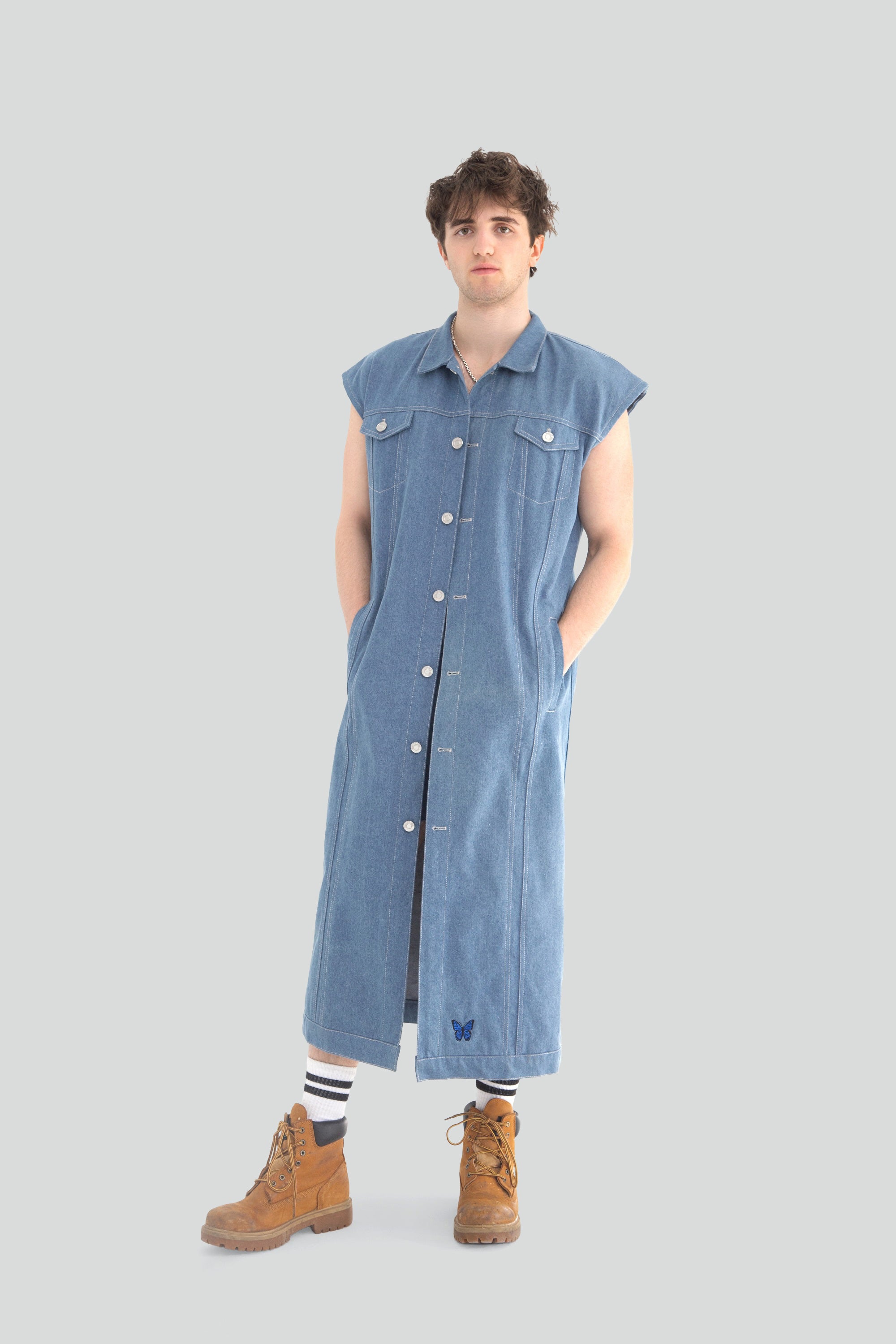 Person wearing a long blue denim vest on a plain background