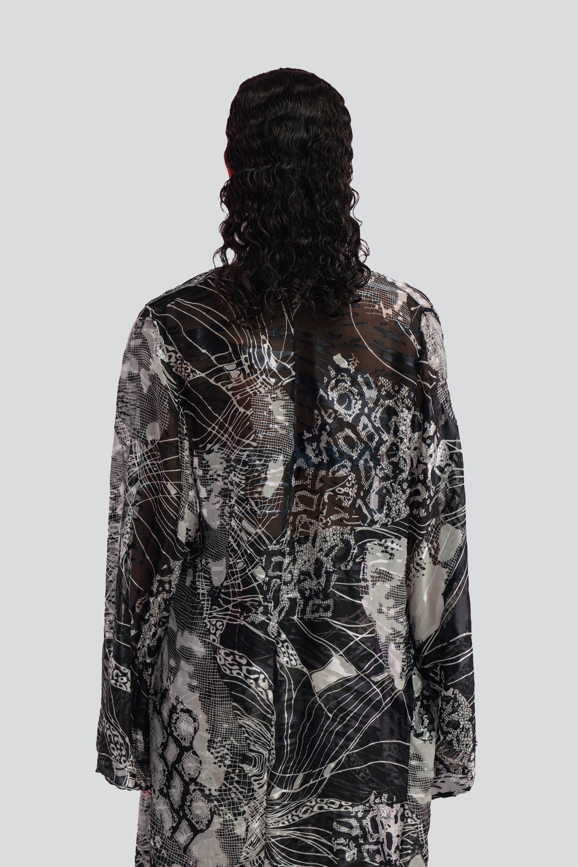 Back view of a woman wearing a long, black and white patterned cover up top on a plain background