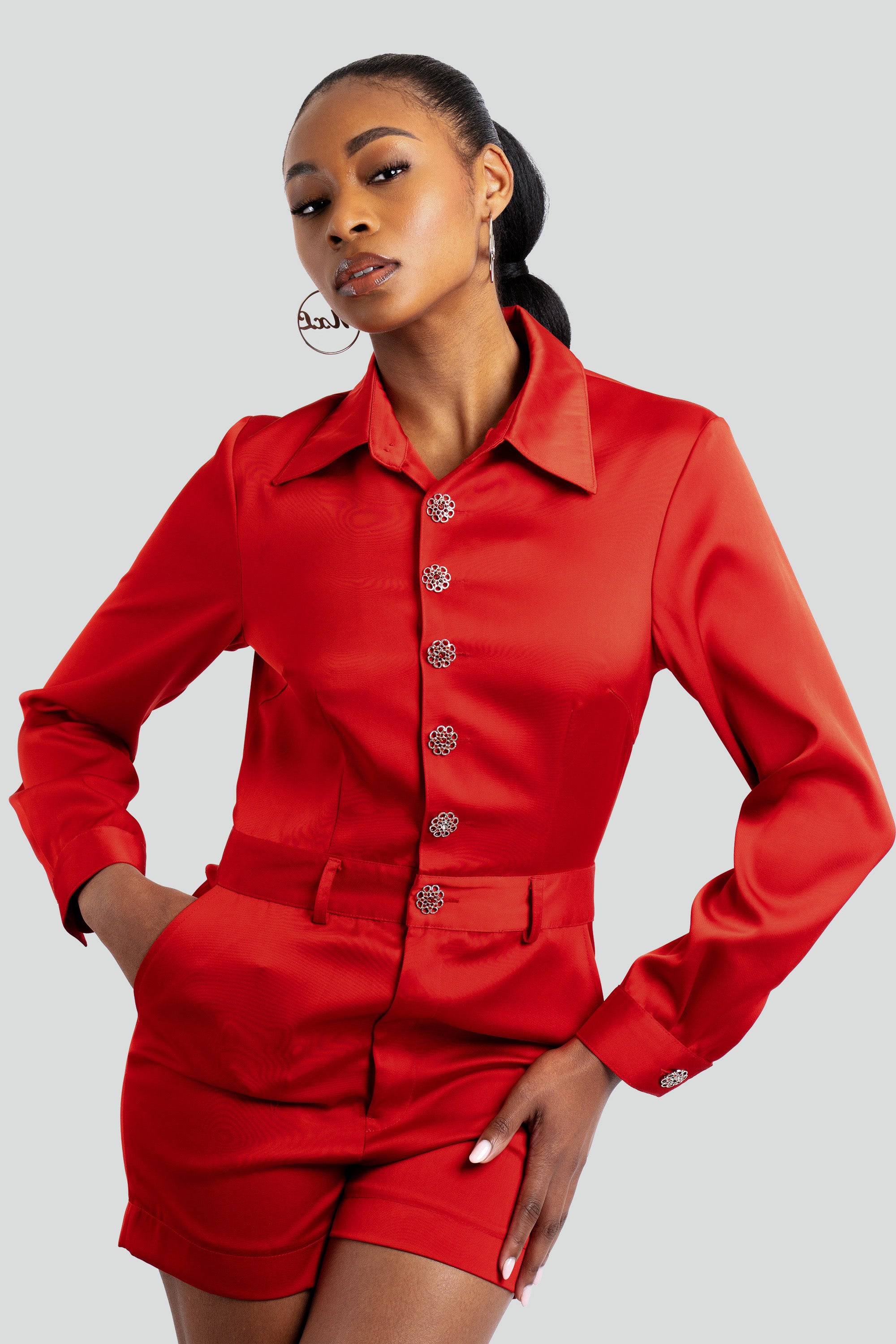 Woman wearing a red satin romper with silver embellishments posing against a white background