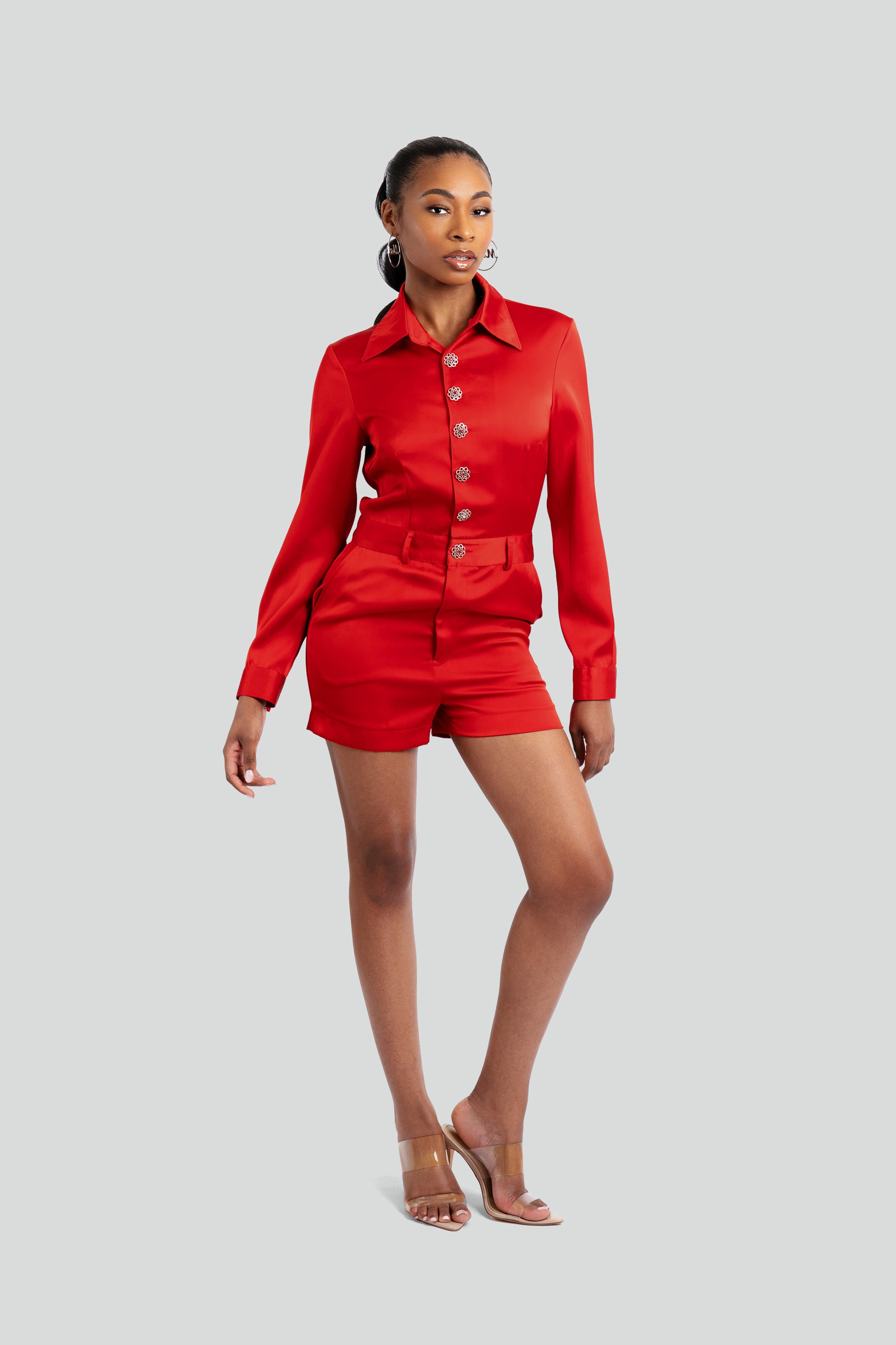 Woman wearing a red satin romper with silver embellishments posing against a white background