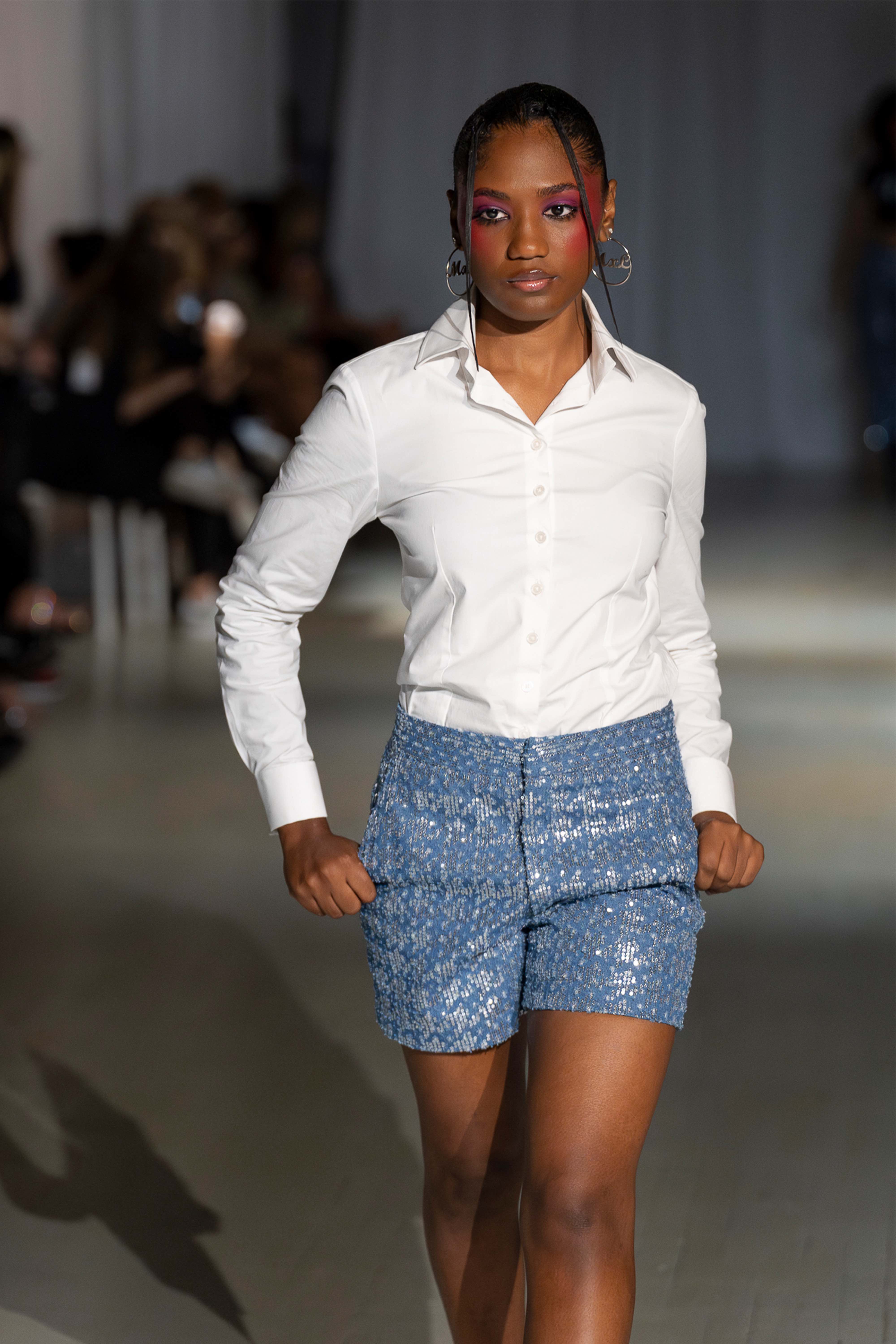 Model wearing high-waisted sequined blue denim shorts with a white button top walking on the runway