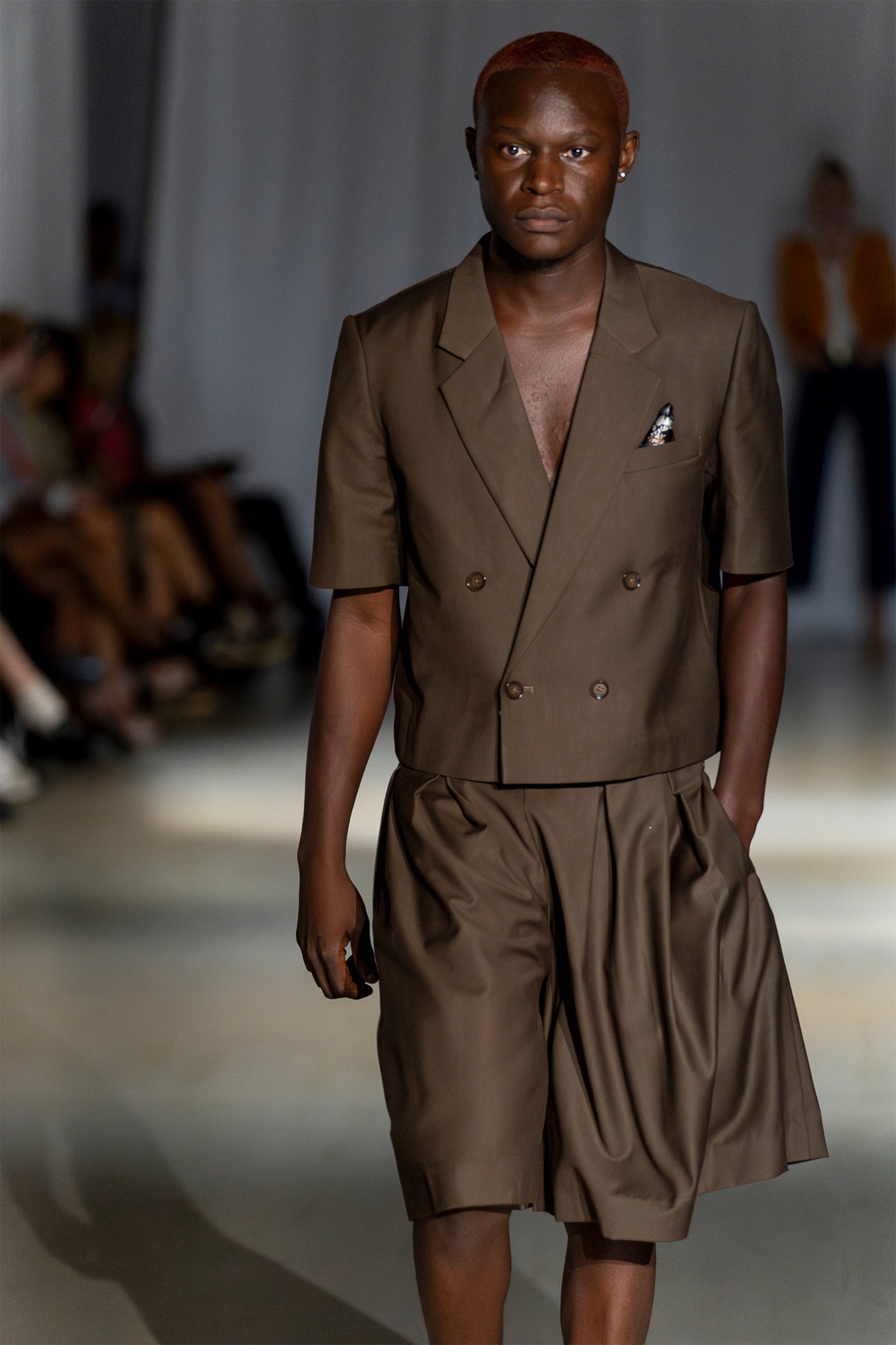 Model wearing a cropped brown blazer and short set walking down the runway.