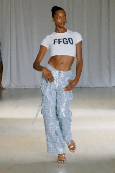 Model wearing a white crop top and sequined cargo pants walking the runway