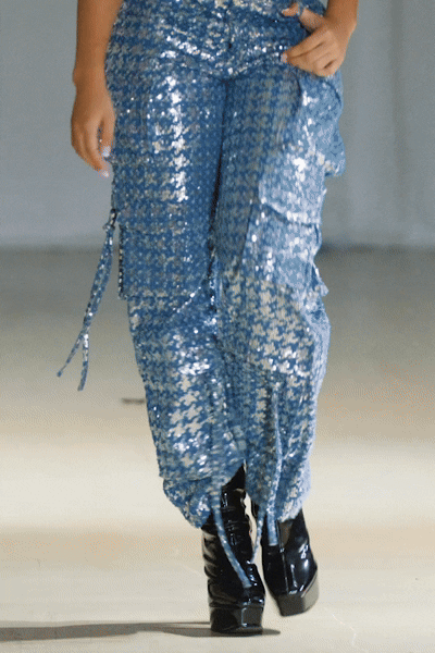 Model wearing a black crop top and sequined cargo pants walking down the runway