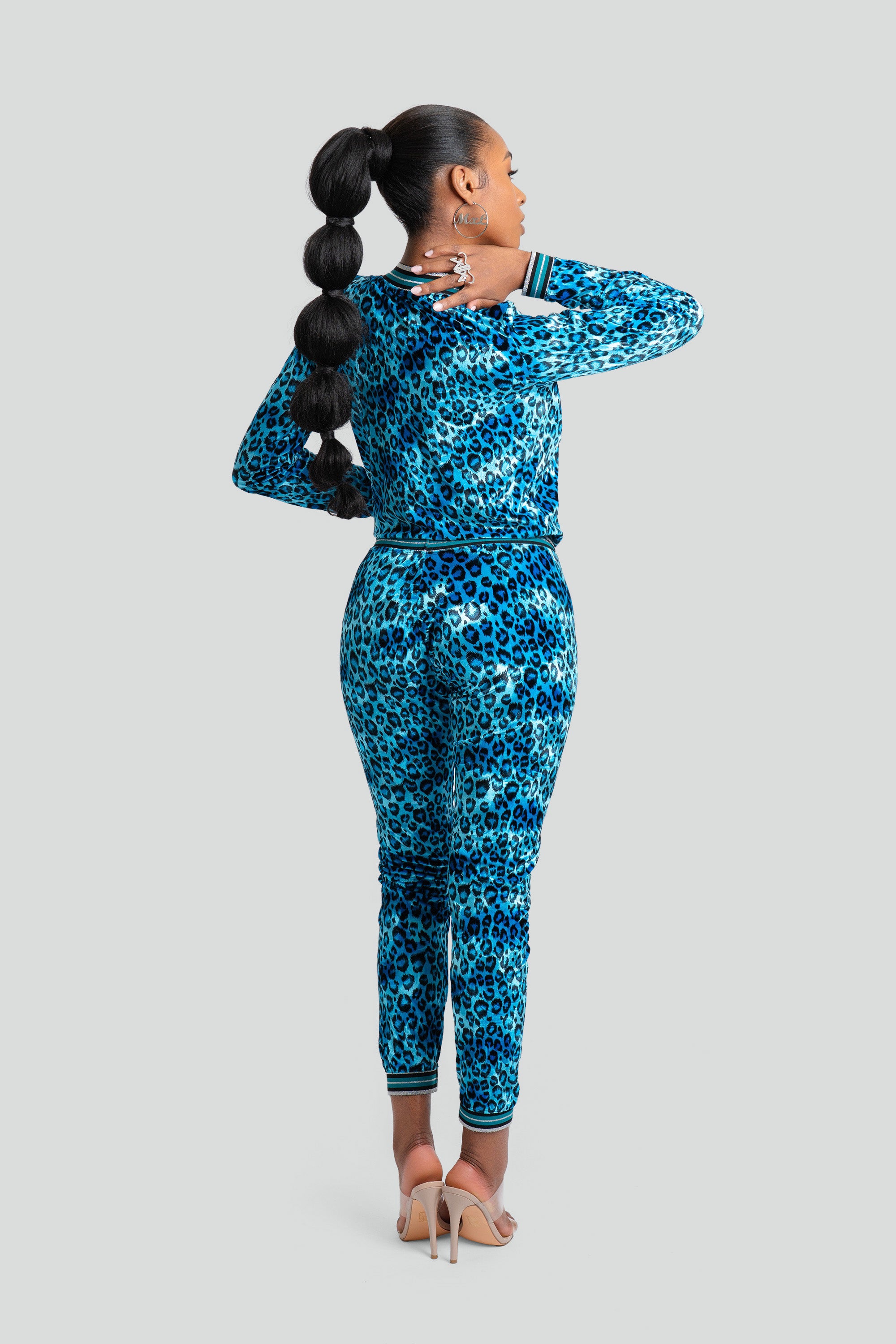 Back view of a woman wearing a blue leopard print velour tracksuit on a white background
