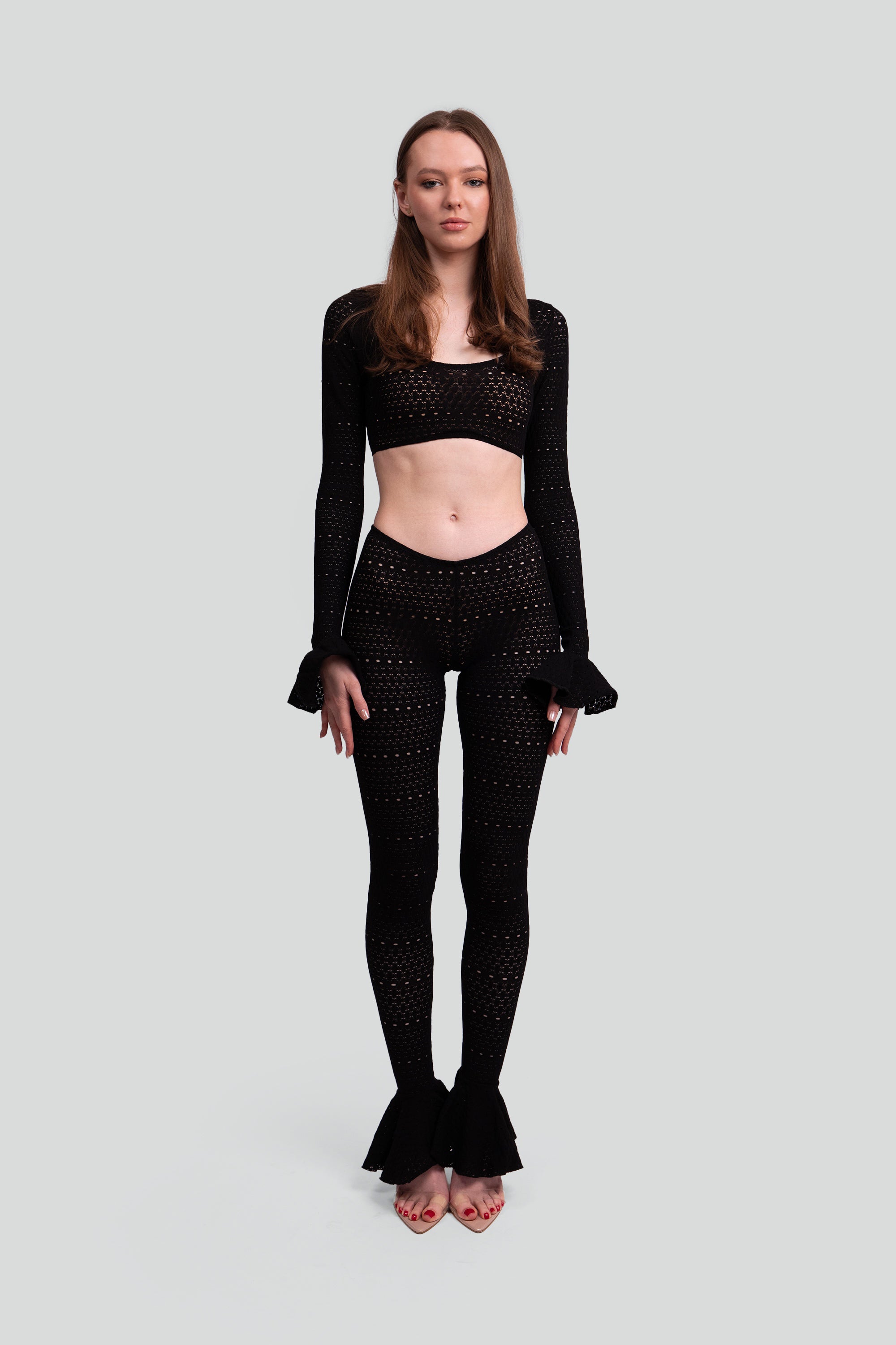Woman wearing a black two piece outfit with ruffled sleeves and leggings on a gray background
