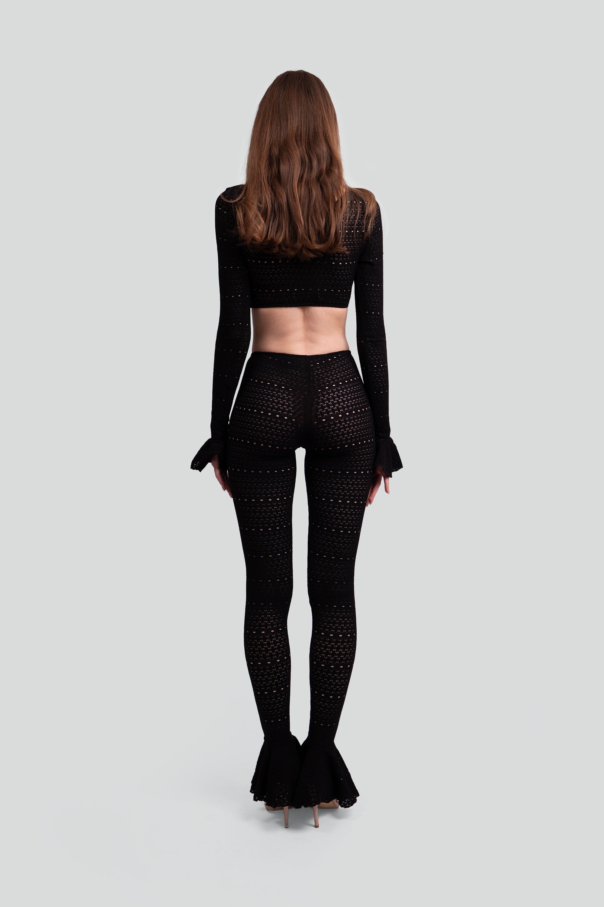 Back view of a woman wearing a black two piece outfit with intricate patterns on a gray background