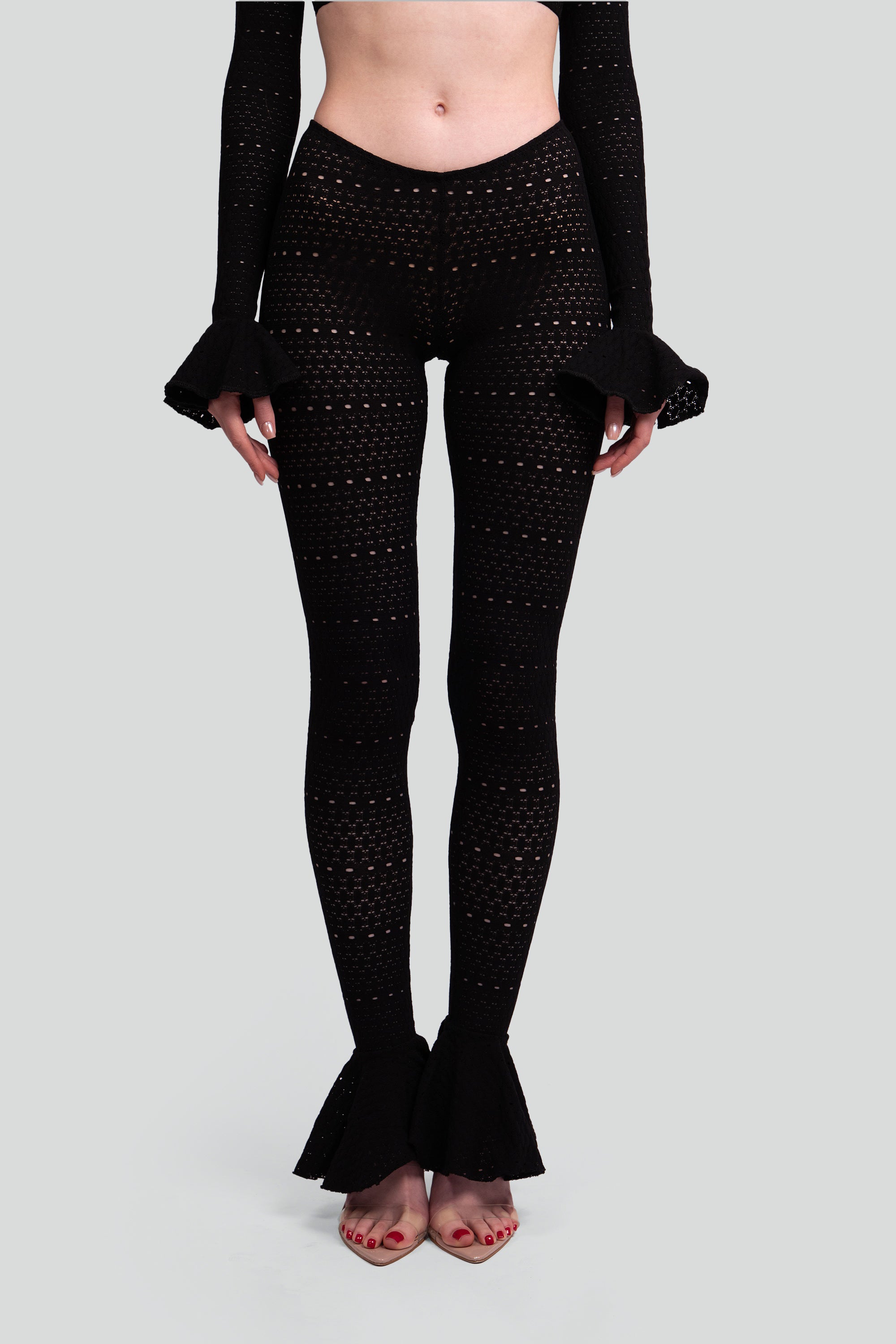 Woman wearing black patterned leggings with flared bottoms on a gray background