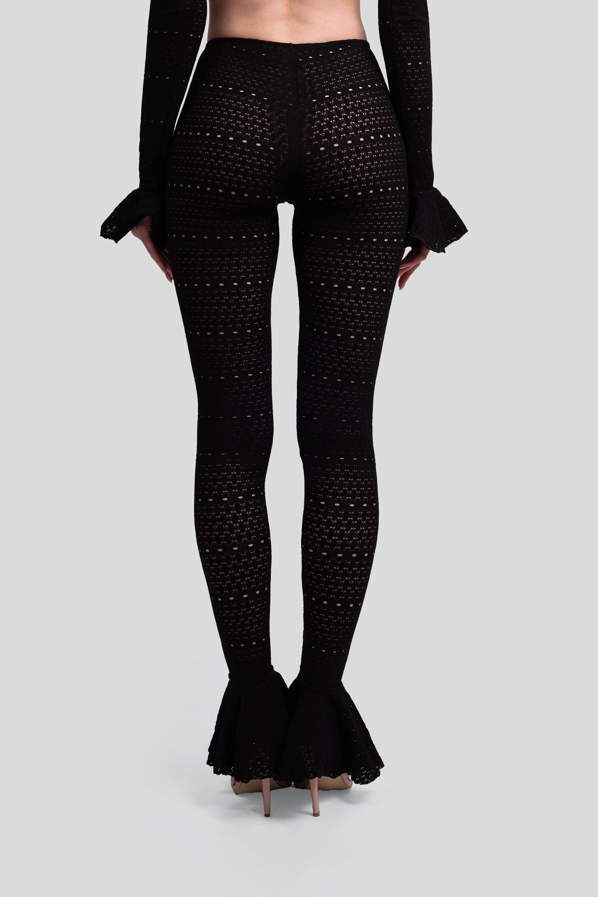 Back view of a woman wearing black patterned leggings with flared bottoms on a gray background
