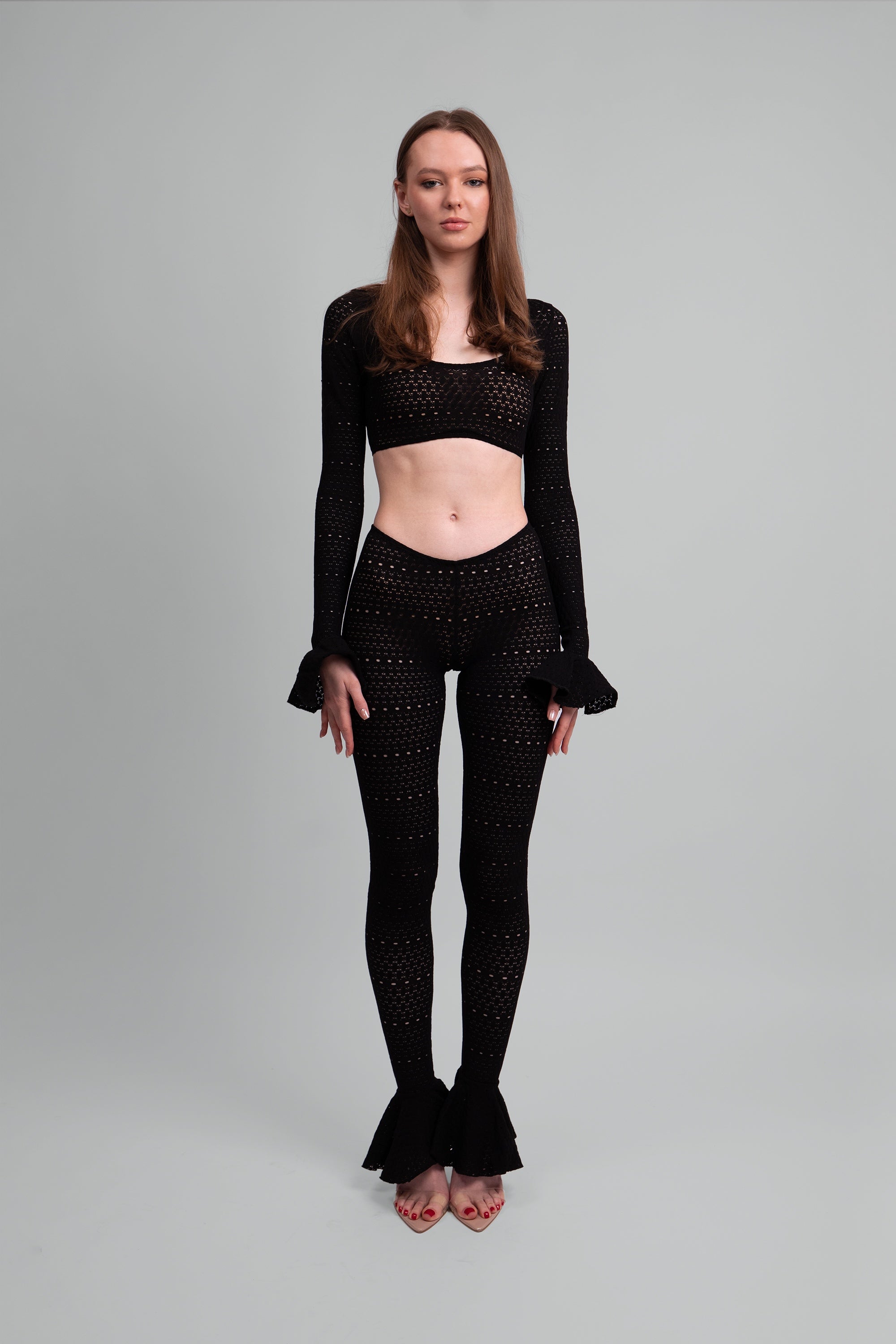Woman wearing a black two piece outfit with ruffled sleeves and leggings on a gray background