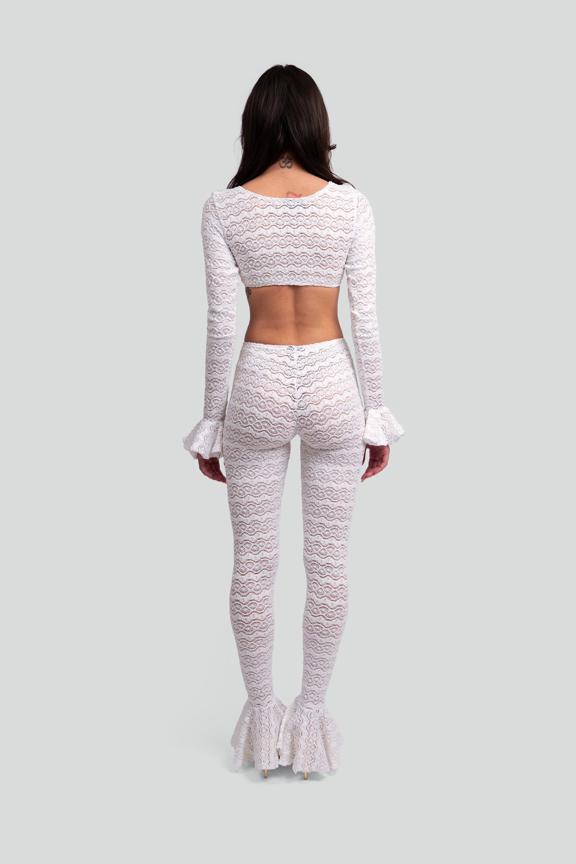 Back view of a woman wearing a white lace outfit on a gray background