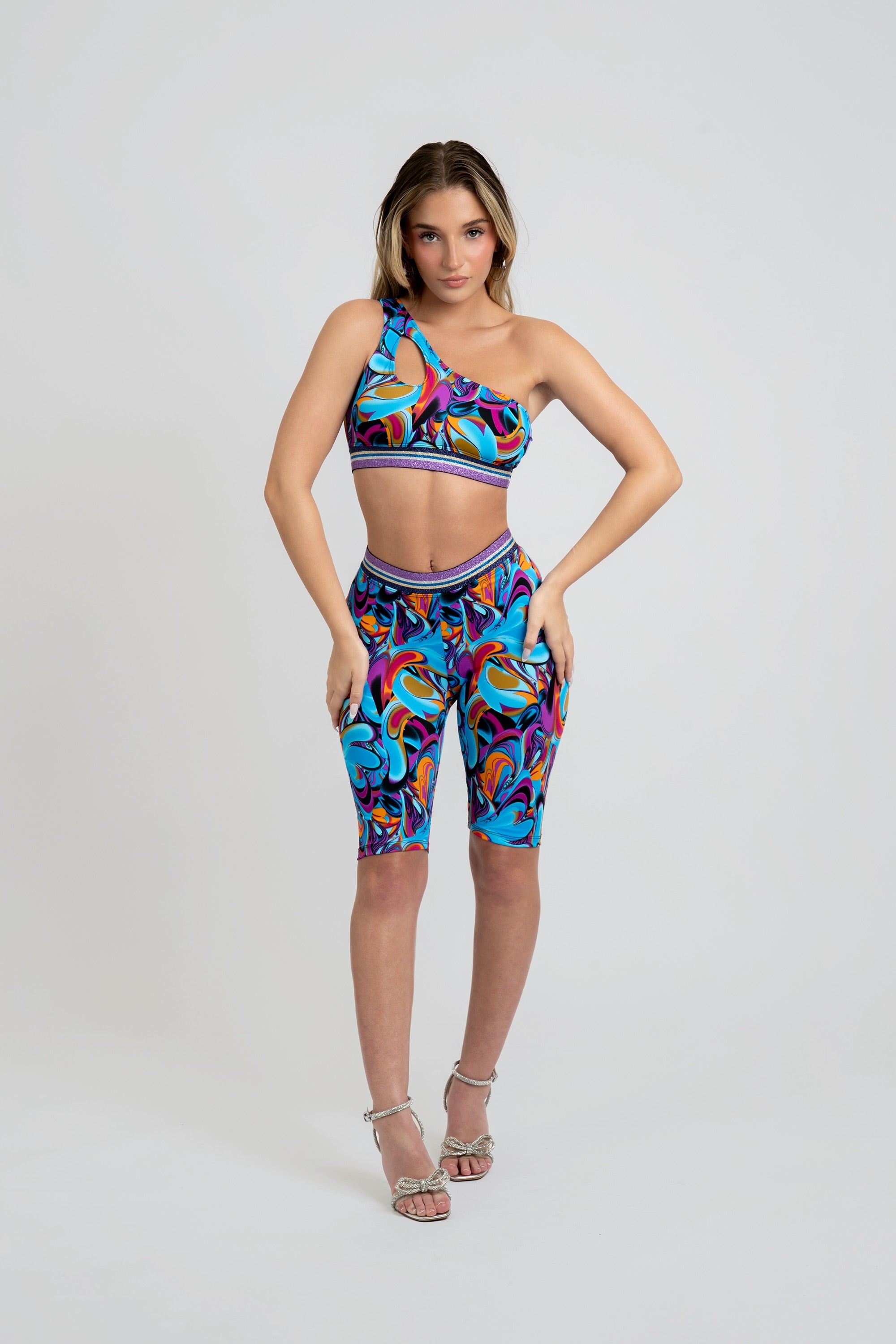 Woman wearing a colorful sports bra and capri leggings with a purple trim on a gray background