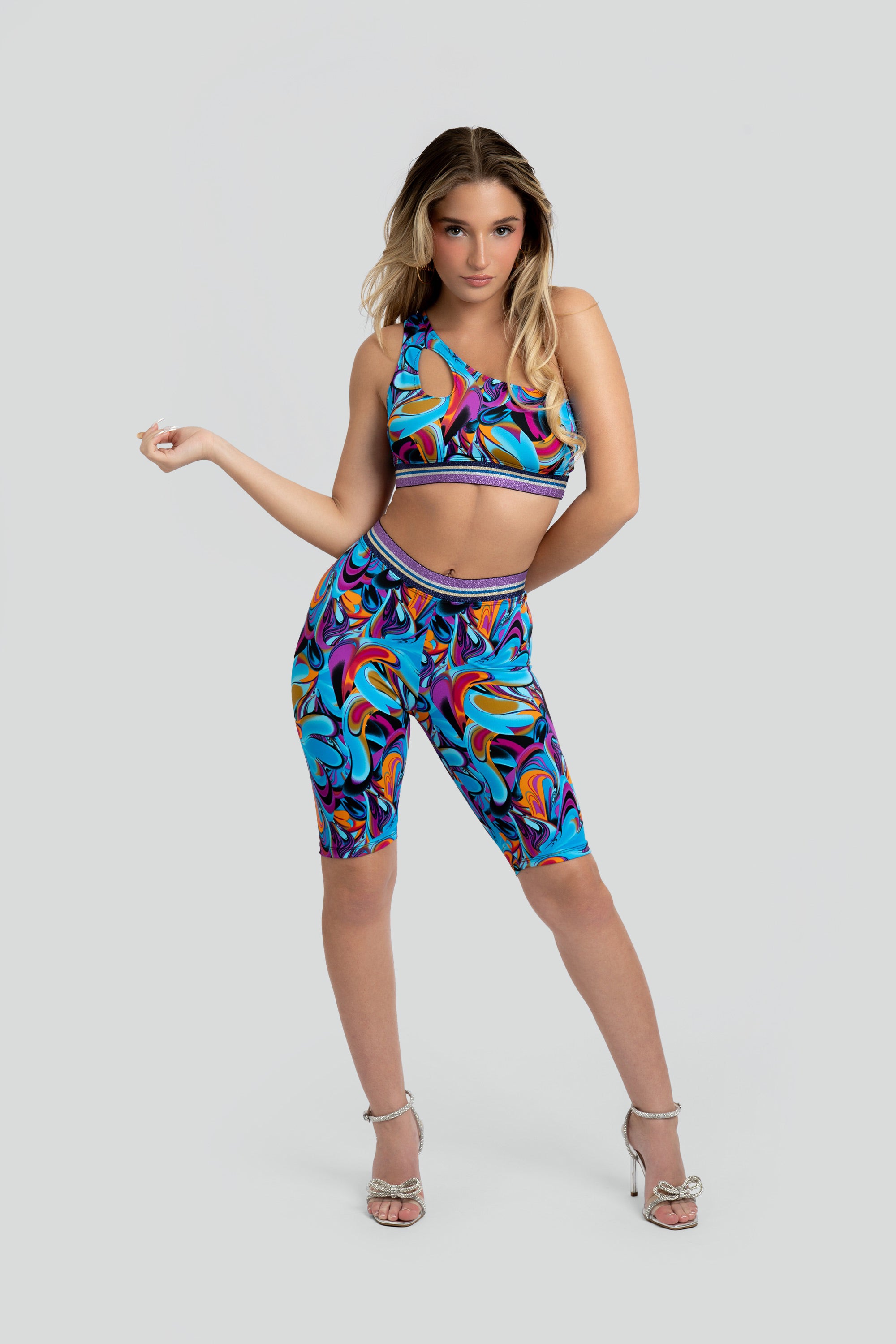 Woman wearing a colorful sports bra and capri leggings with a purple trim on a gray background