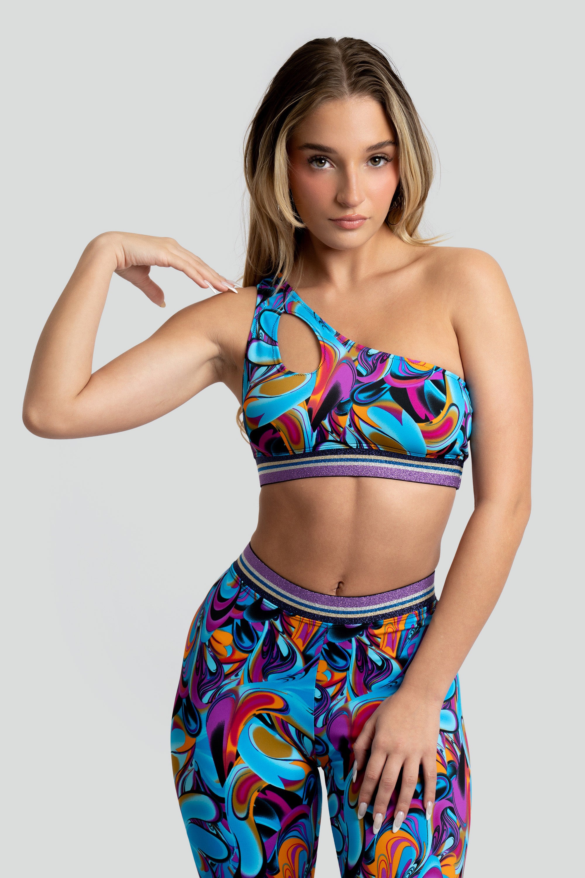 Woman wearing a colorful sports bra and capri leggings with a purple trim on a gray background