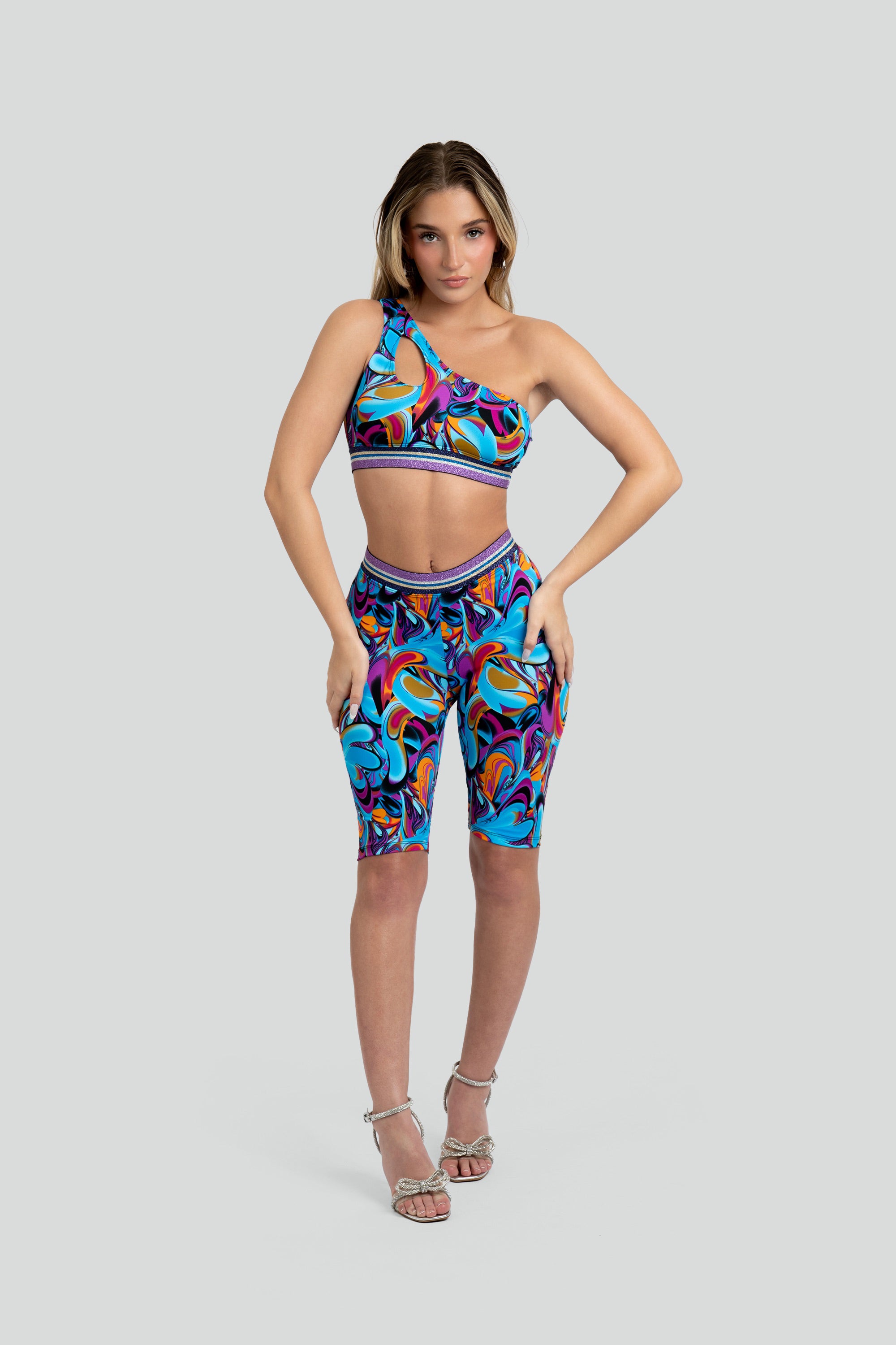 Woman wearing a colorful sports bra and capri leggings with a purple trim on a gray background