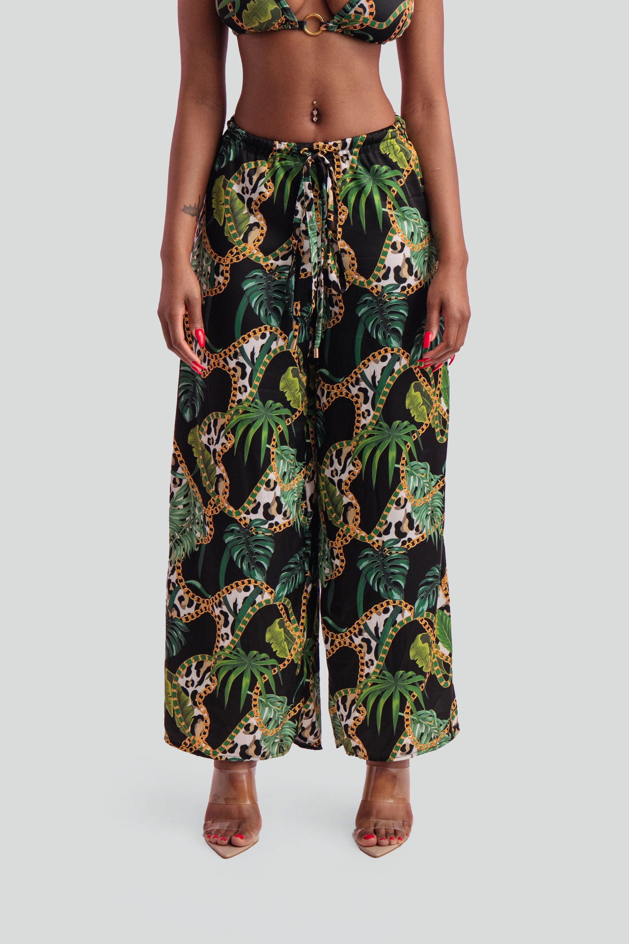 Woman wearing a tropical print bikini and wide leg pants on a gray background