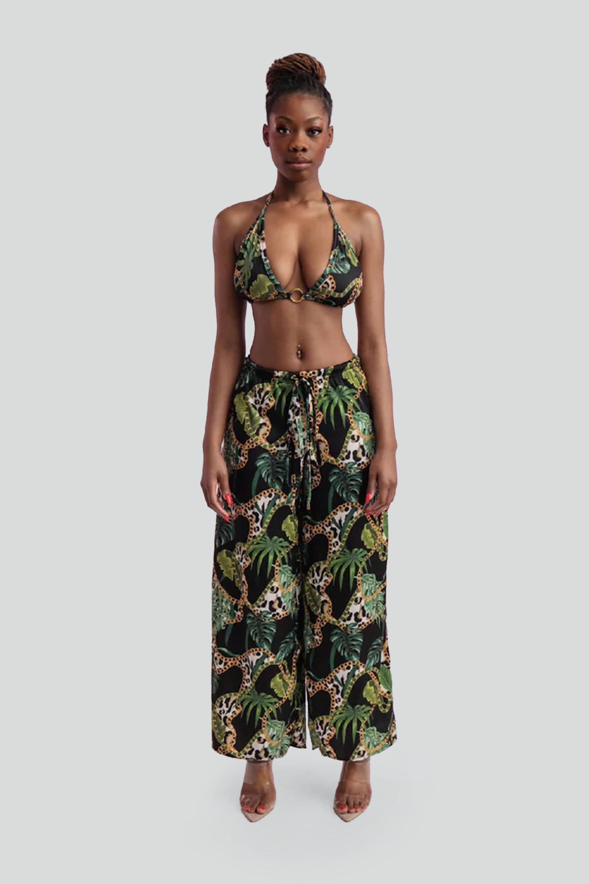 Woman wearing a tropical print bikini and wide leg pants on a gray background