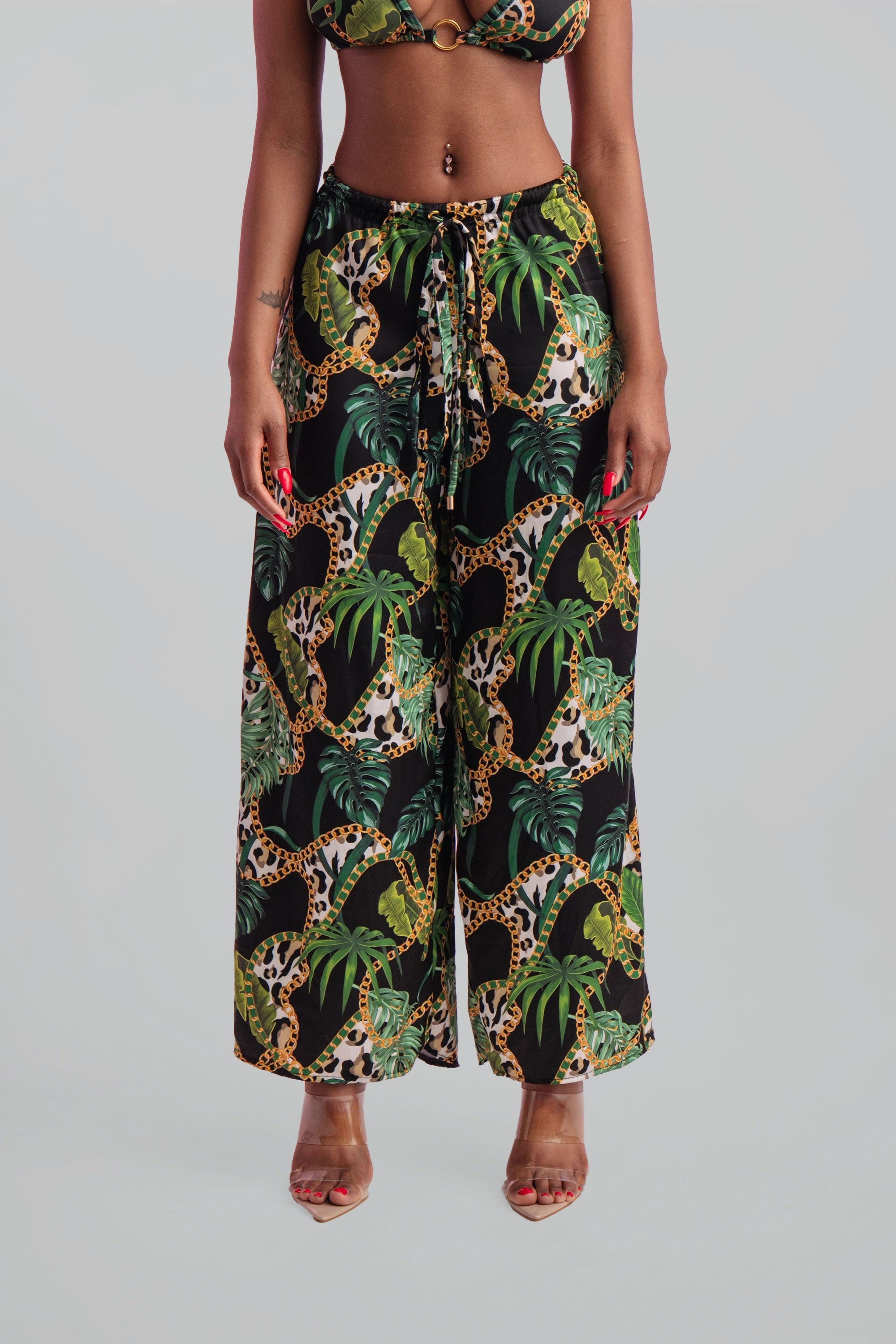 Woman wearing a tropical print bikini and wide leg pants on a gray background