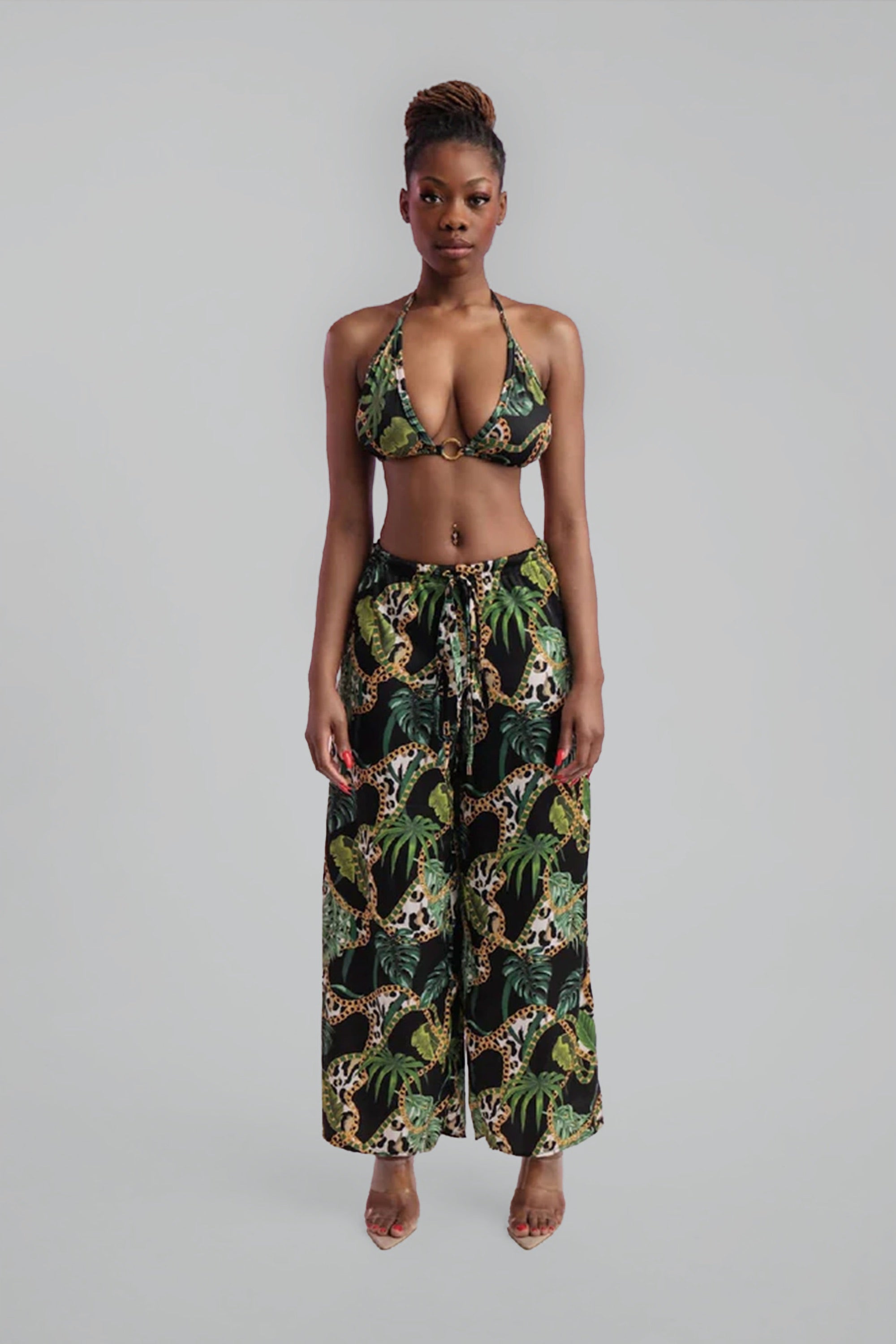 Woman wearing a tropical print bikini and wide leg pants on a gray background