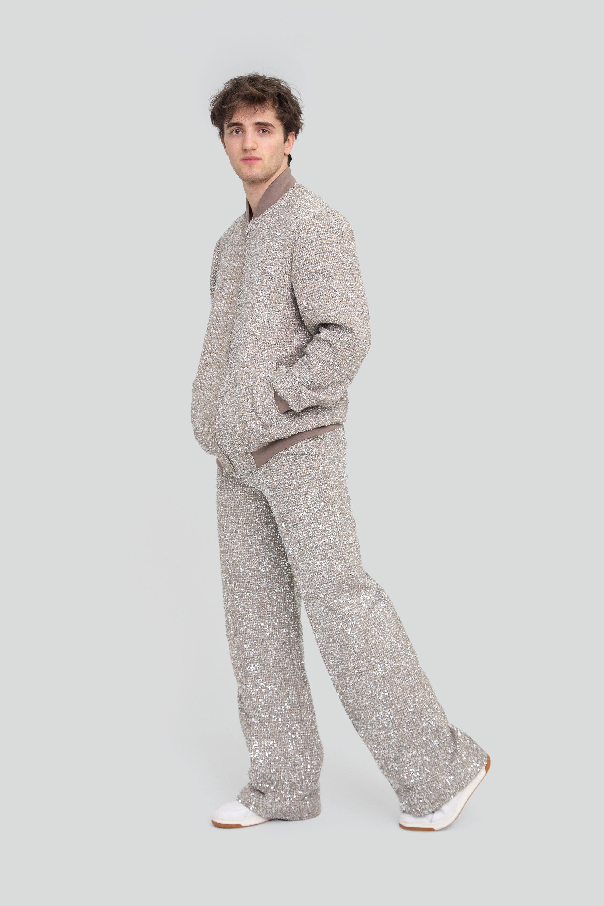 Man wearing a sparkling silver outfit with sequin pants on a plain background