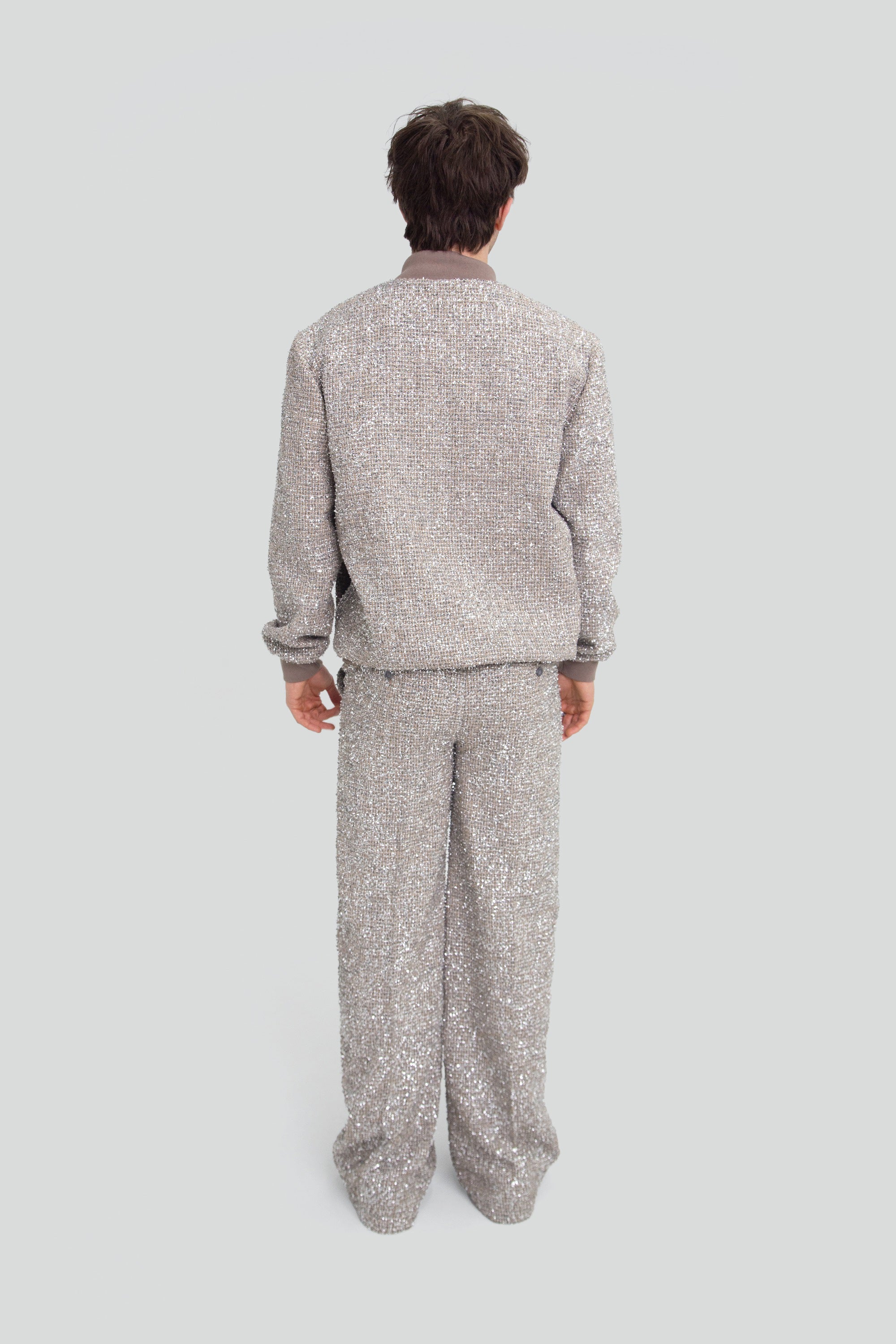 Back view of a man wearing a sparkling silver outfit with sequin pants on a plain background