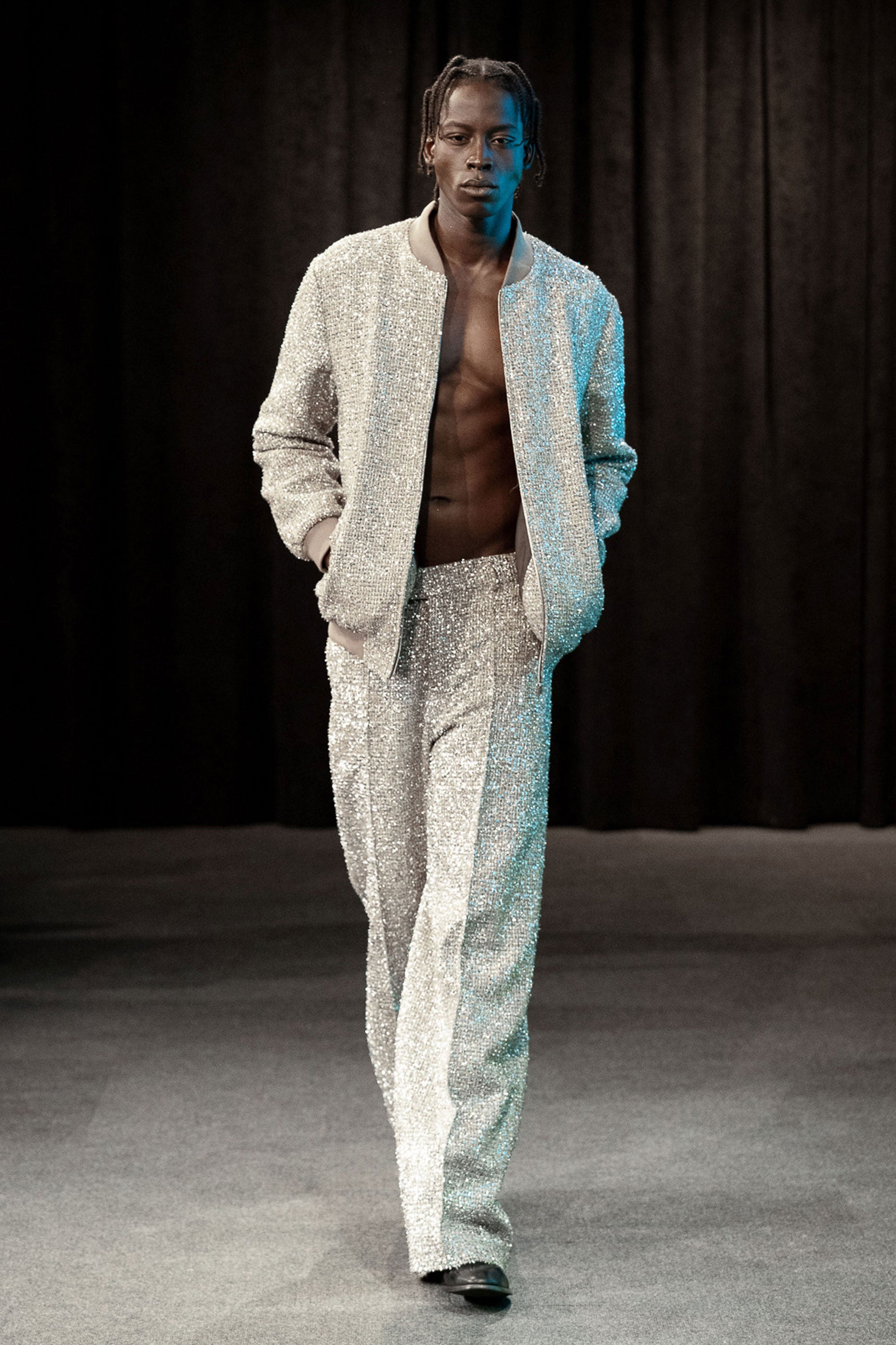 Man wearing a light-colored textured metallic tweed outfit on a dark background