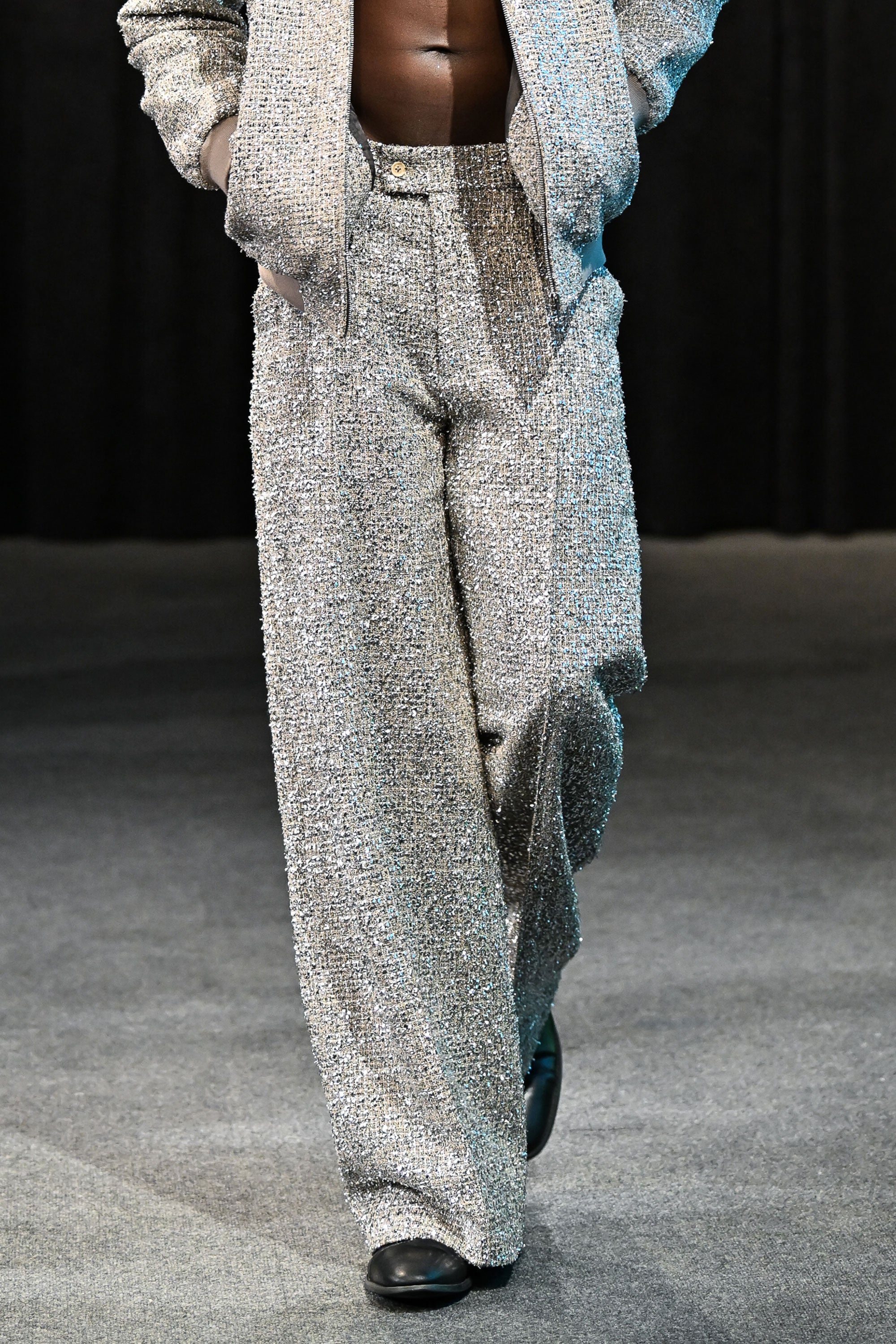 Person wearing a textured metallic tweed gray outfit with wide-leg pants on a runway.