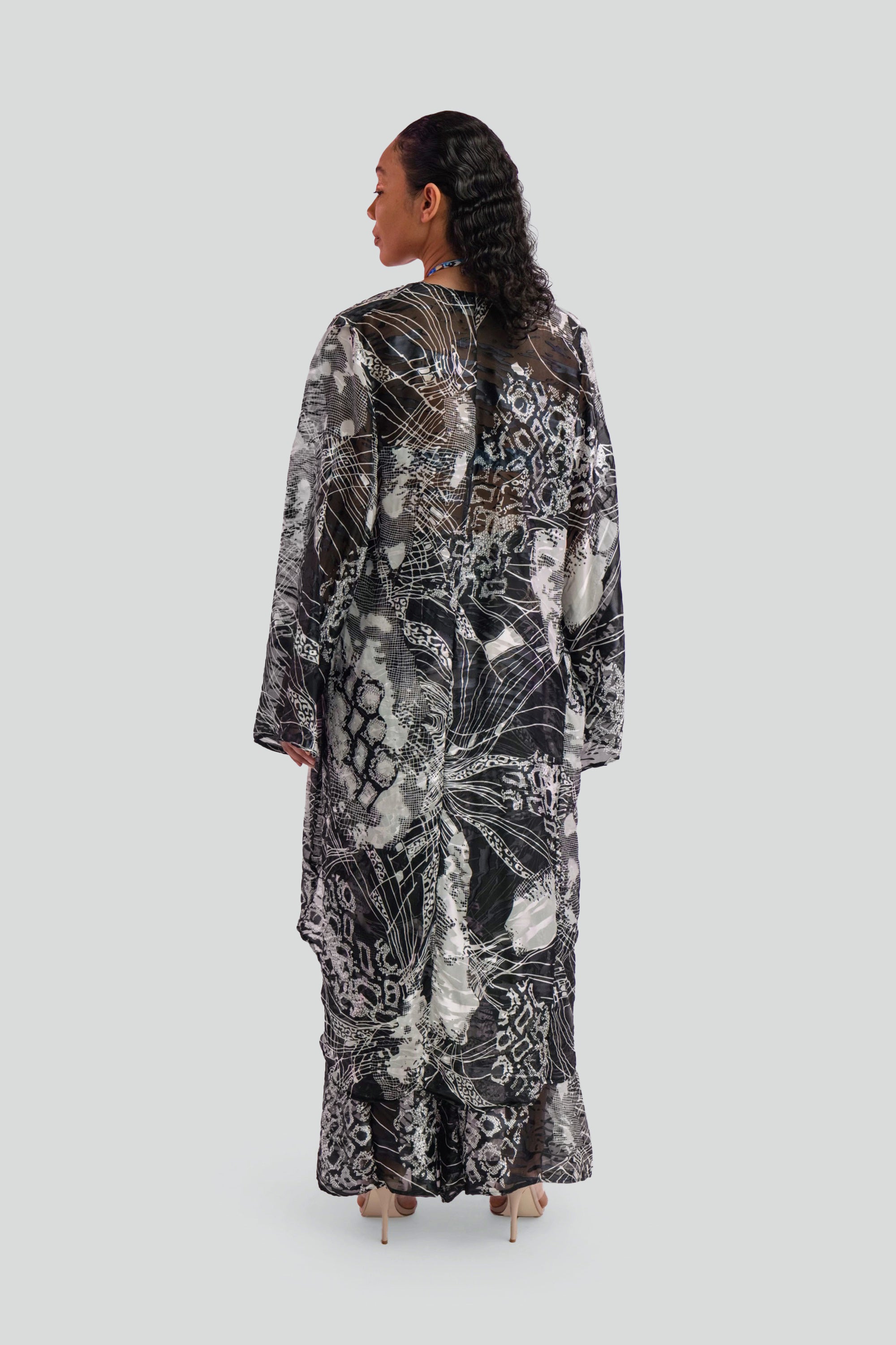 Woman wearing a long, black and white patterned cover up top on a plain background