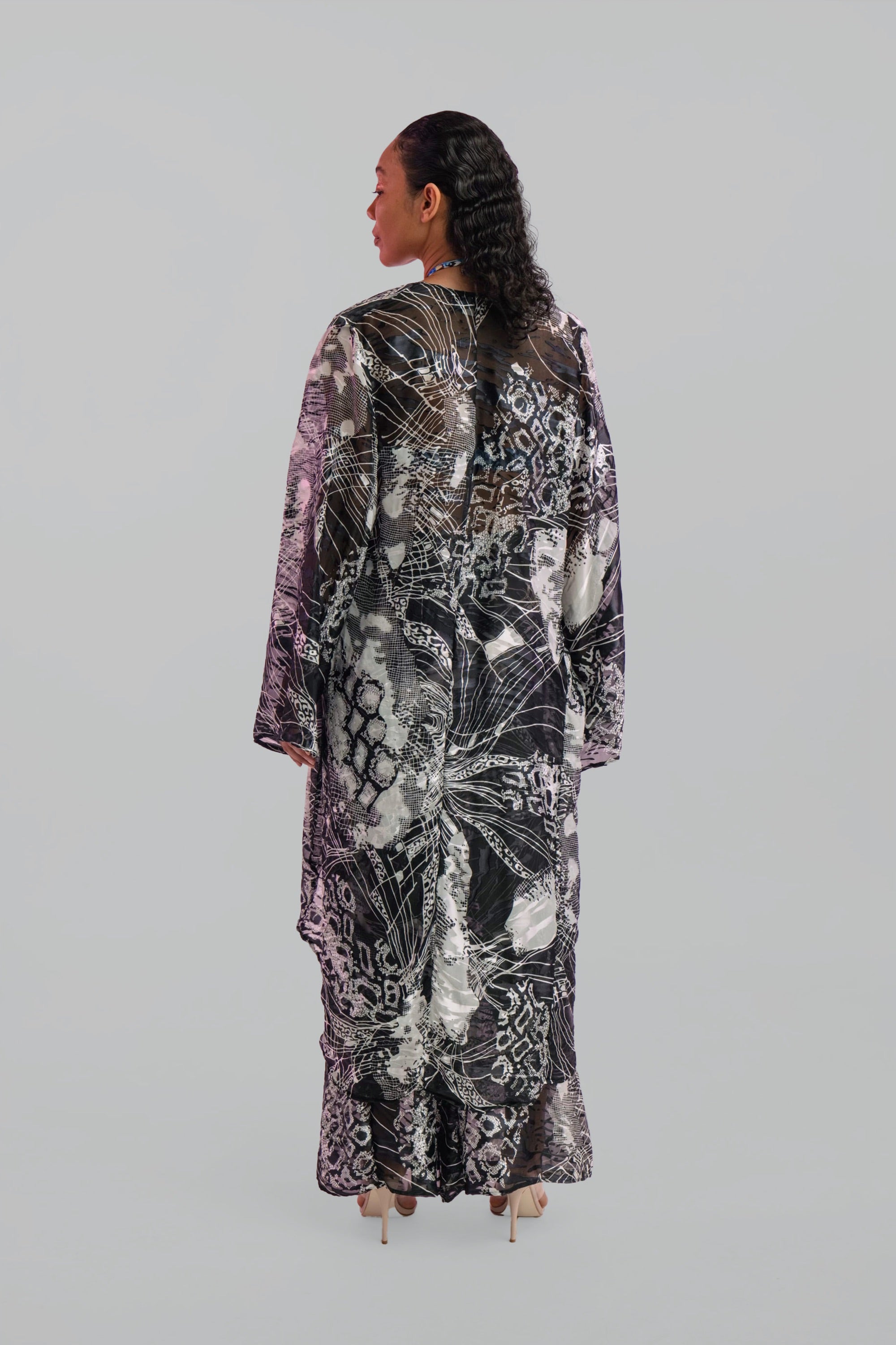 Woman wearing a long, black and white patterned cover up top on a plain background