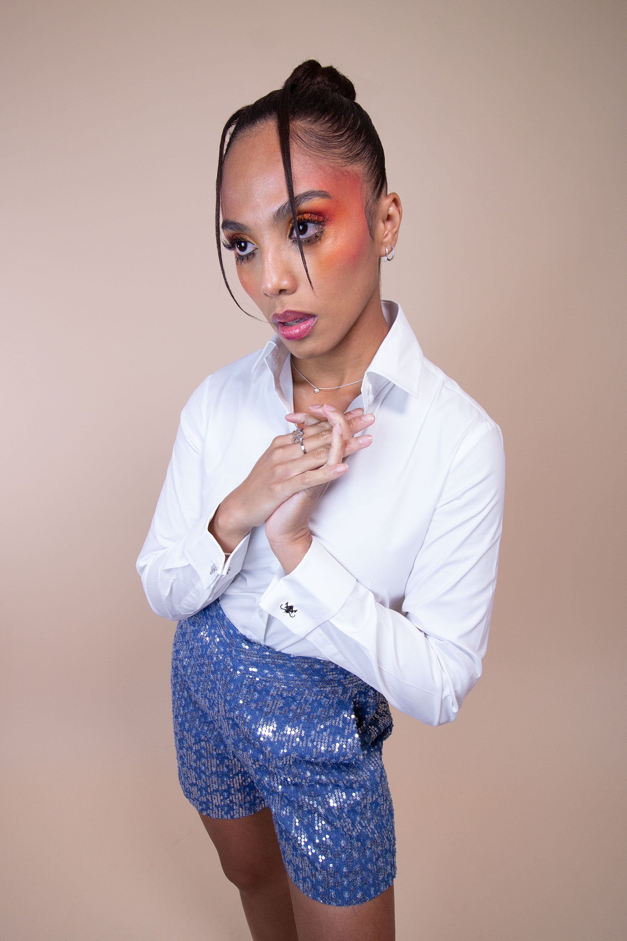 Woman wearing high-waisted sequined blue denim shorts with a white button top posing against a light background