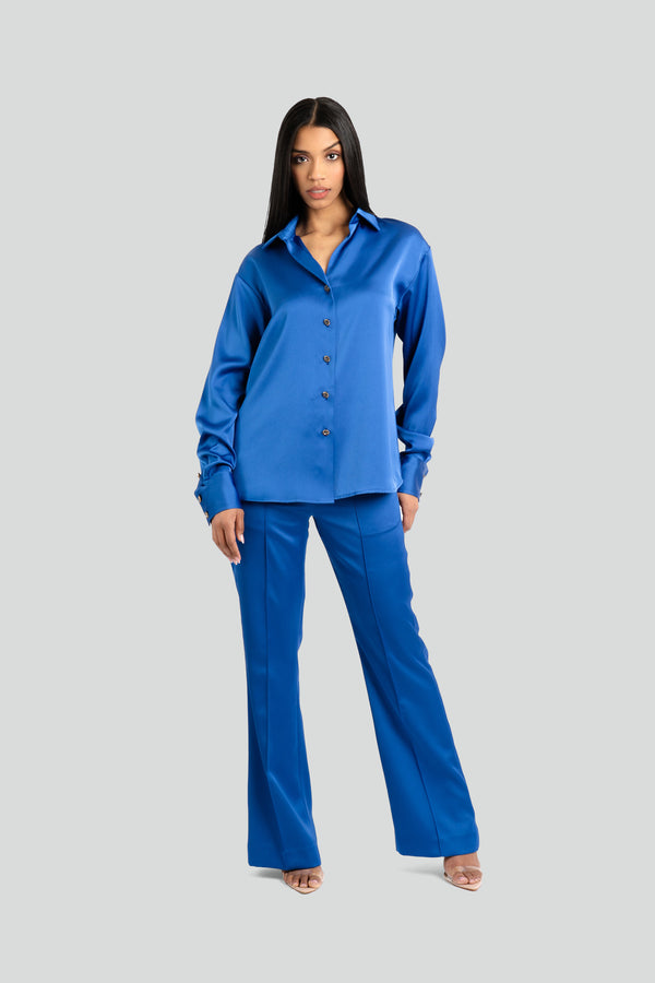  Two-piece women's pajama-style suiting set in a lustrous royal blue satin, featuring a relaxed button-down shirt and mid-rise wide-leg trousers