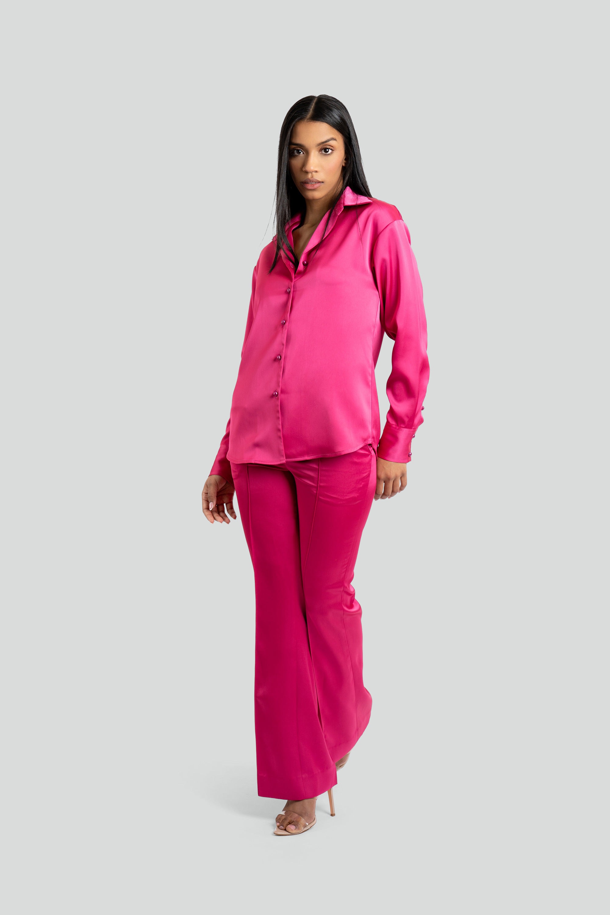 Woman wearing a bright pink satin shirt and pants set on a white background