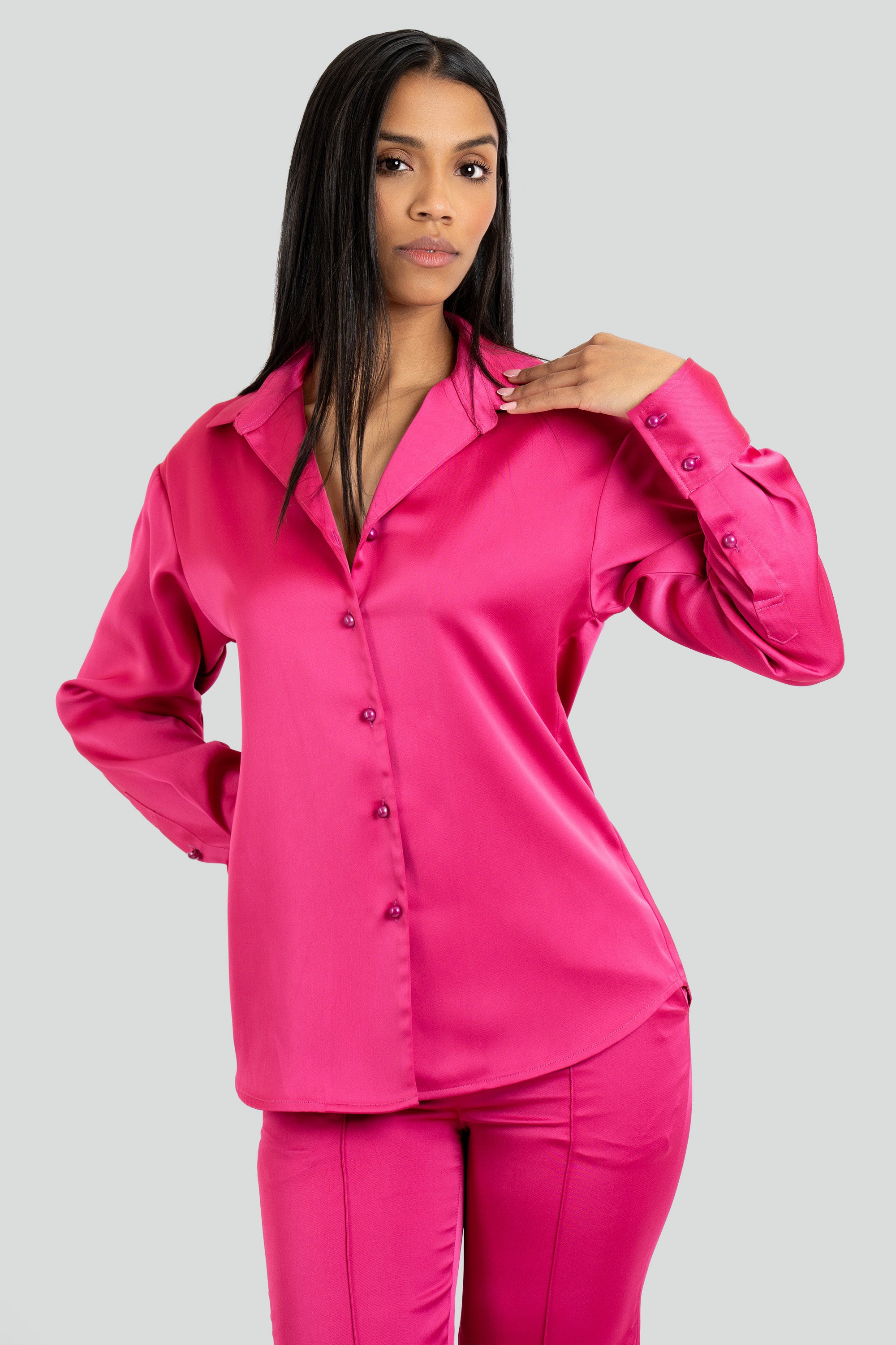 Woman wearing a bright pink satin shirt and pants set on a white background